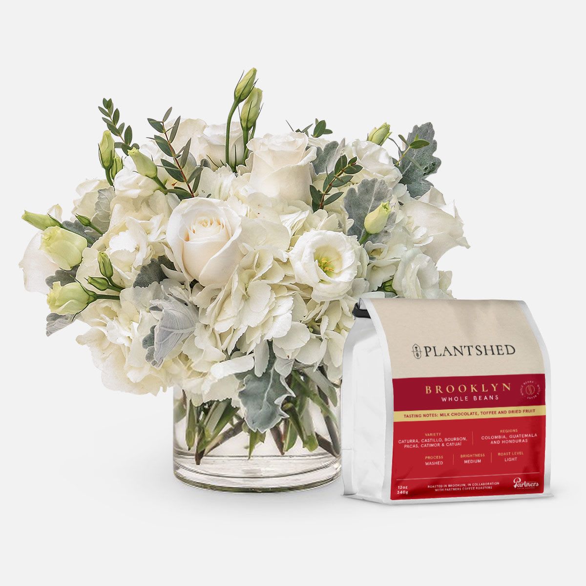 Emily + PlantShed Coffee [Brooklyn - Whole Beans] - [ Flower Arrangement Height: 10'' - 11'' | Diameter: 10'' - 11" ] The Emily is paired with the PlantShed Coffee Blends – the perfect bundle for true coffee enthusiasts! The floral arrangement features a lovely mix of white flowers. Roses and lisianthus are tucked into clouds of hydrangeas, while soft dusty miller and fresh greens provide texture and fullness. Clean and pure, Emily is an elegant addition to any table.  PlantShed has been your local Manhattan florist for more than 35 years.