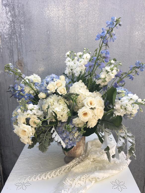 The Michele - This classic arrangement is perfect for any individual with blue and white hydrangeas, delphinium, white roses and greenery in a gorgeous marble mercury glass compote vase or a white ceramic pedestal vase.