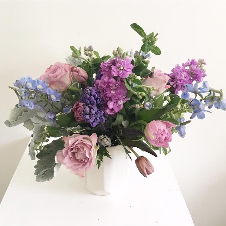 The Violette - This medium-sized arrangement is as sweet as sugar, with varying shades of blues and purples. Blue tweedia, purple stock, hyacinths, moody roses, dusty miller, and even hints of chocolate-brown tulips come together to create a fresh and enchanting twilight-inspired floral display.