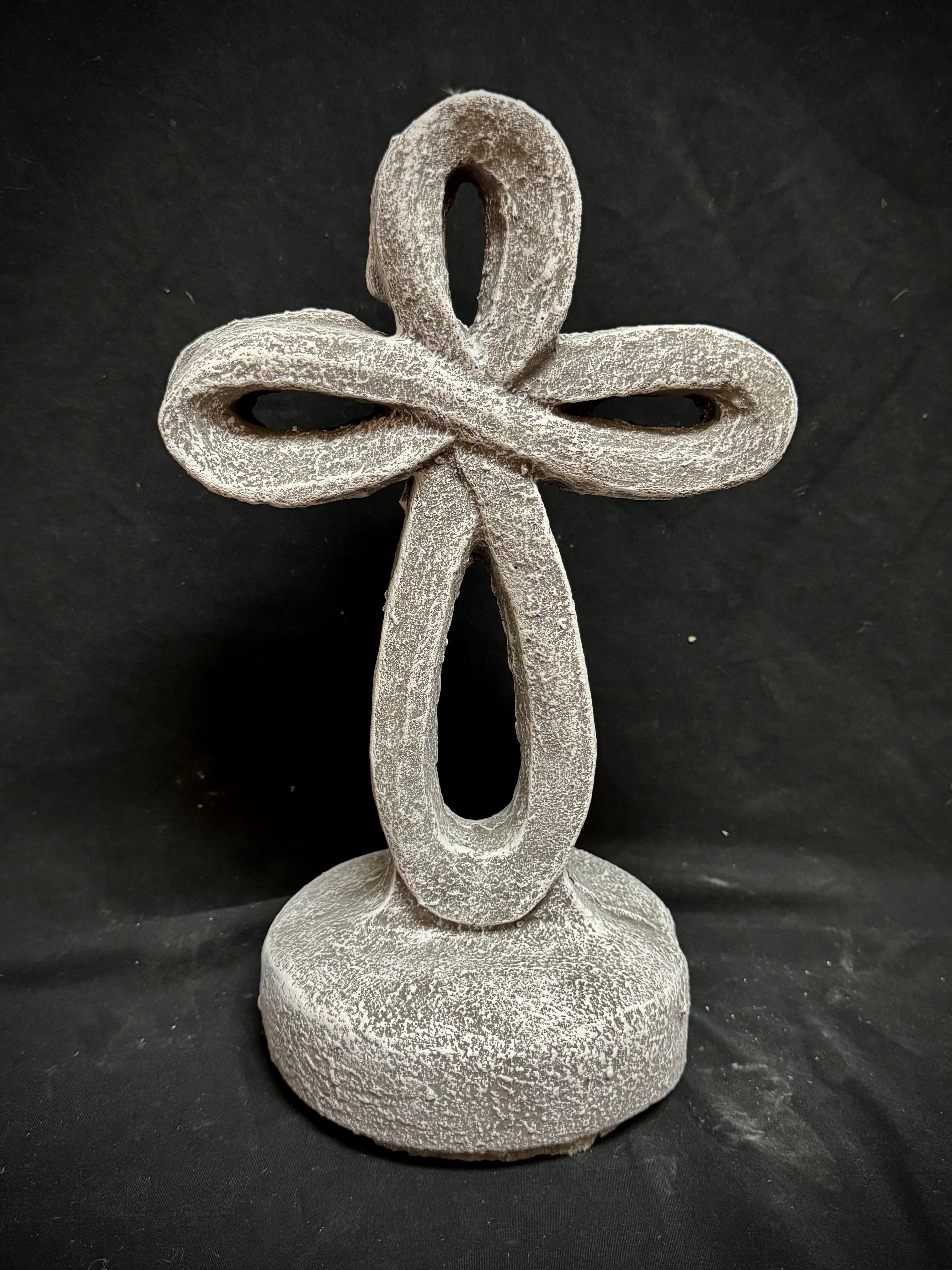 12 Inch Eternity Cross - Our 12-inch cement eternity cross is a beautifully crafted symbol of faith and remembrance. Made from durable, weather-resistant cement, it features a timeless design with smooth edges and a sturdy structure. The eternity cross, characterized by its continuous, unbroken form, represents everlasting life and spiritual devotion. Its neutral gray tone complements any setting, whether placed in a garden, memorial site, or indoor display. Designed to withstand the elements, this piece serves as a lasting tribute to faith, love, and eternity. Available in two colors tan and stone with white wash. Crosses will be decorated with a bow under the stand price. Silk flowers will be added to the deluxe. 