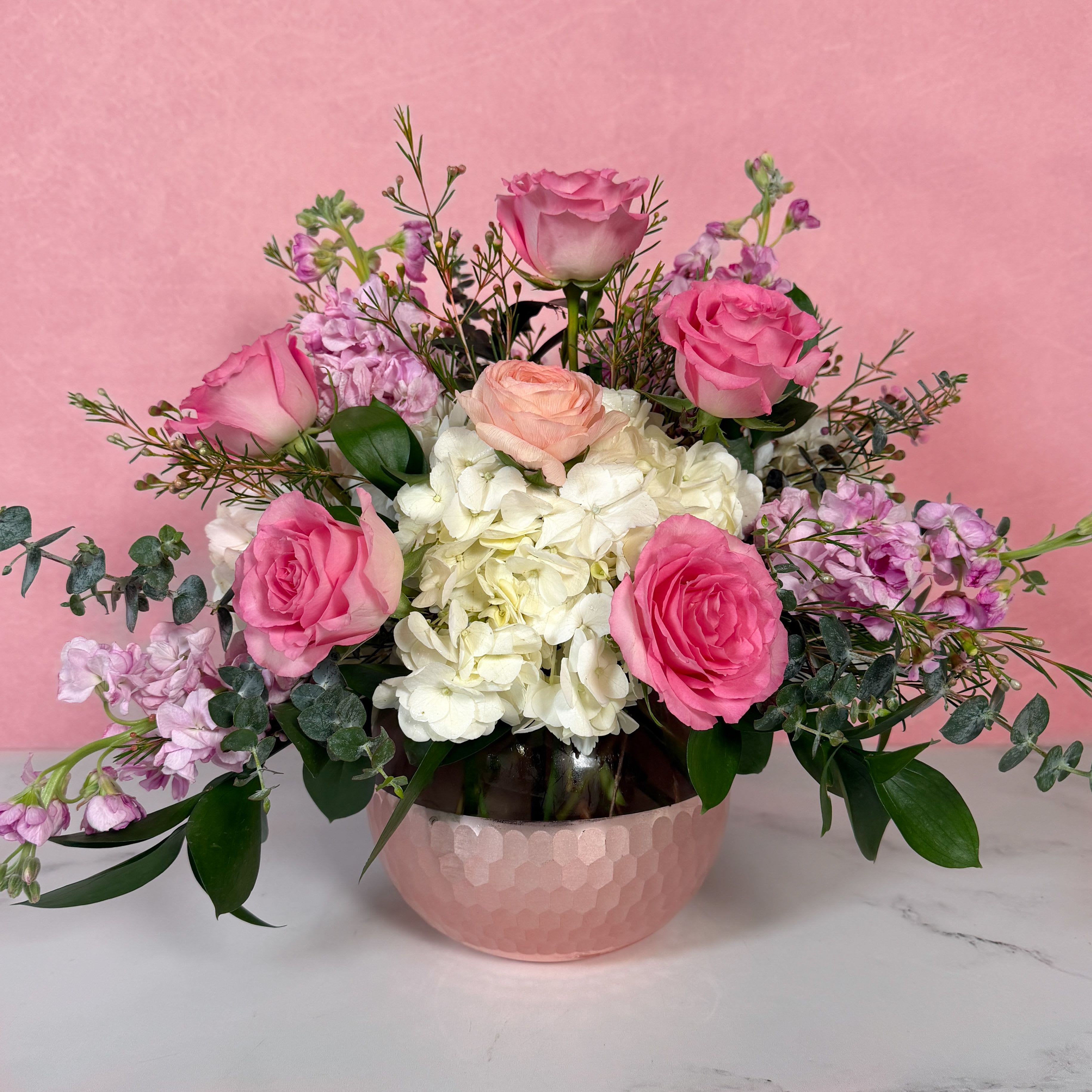 Vogue Valentine - Get your Valentine an arrangement as stylish as they are! Vogue Valentine is a classy, modern design, with pink roses, peach ranunculus, pink stock, white hydrangea, and perfect filler flowers artfully crafted in a dazzling rose gold glass bowl. This arrangement would make an incredible gift for anyone with a love of all things chic, and is sure to be a showstopper this Valentine's Day!  Approx. L 19" x H 15"