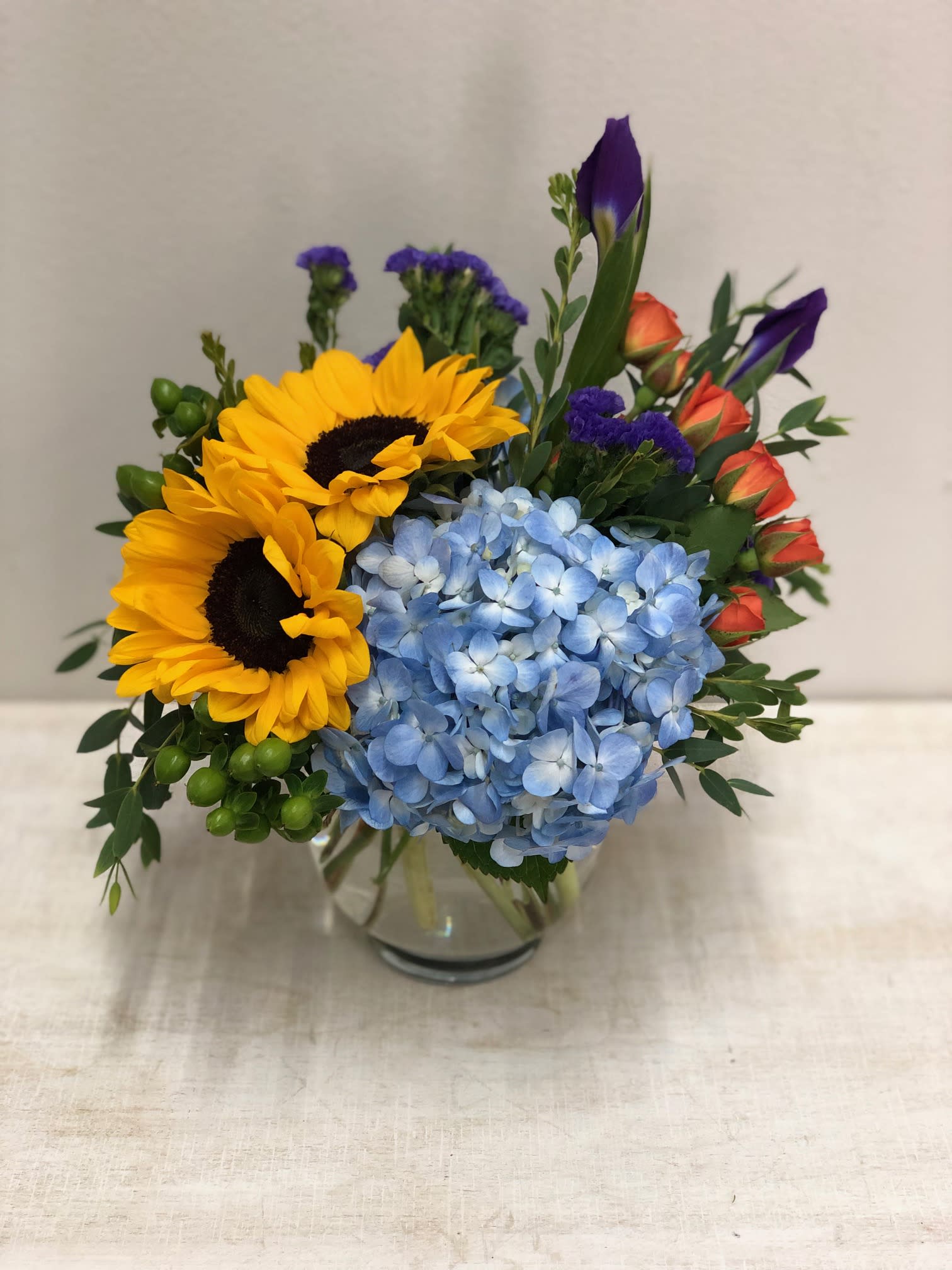 Sunny Days - Perfect for a desk, this summery and bright arrangement will brighten up their day!  Small bubble bowl arrangement, short/compact, of spray roses, hydrangeas, sunflowers and iris. 