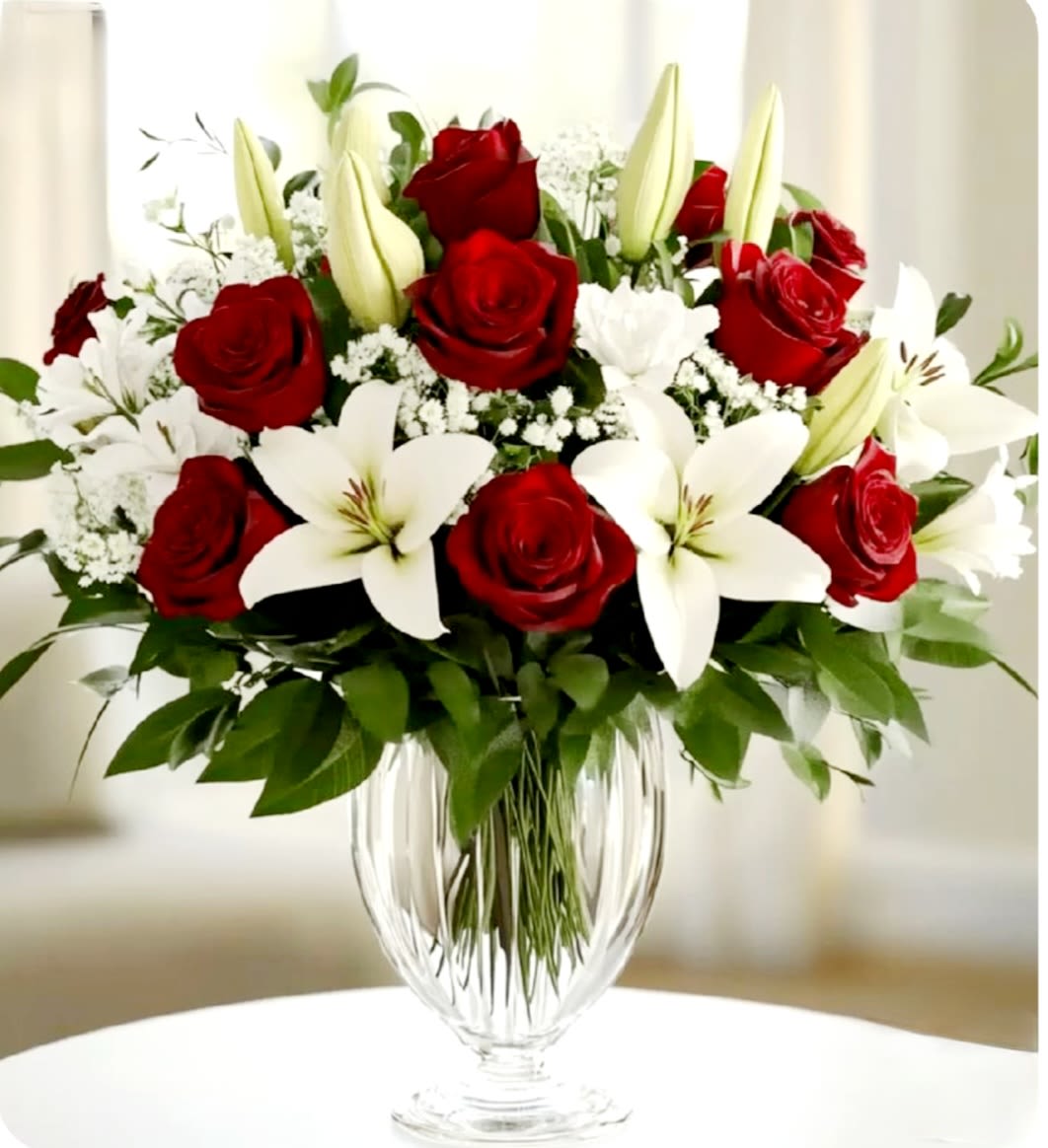 Doir by Pretty in Petals  - This arrangement features red roses, white lilies, and small white filler flowers, all set in a clear glass vase. The bouquet is symmetrical and lush, with green foliage adding contrast and fullness. The combination of deep red and crisp white creates a classic, elegant presentation suitable for formal and romantic occasions.