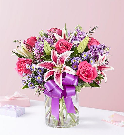 Straight from the Heart - This arrangement with hot pink roses, pink Stargazer lilies, lavender stock, purple waxflower and monte casino; accented with assorted greenery Artistically designed in a clear glass cylinder vase accented with a purple satin ribbon; measures 8"H
