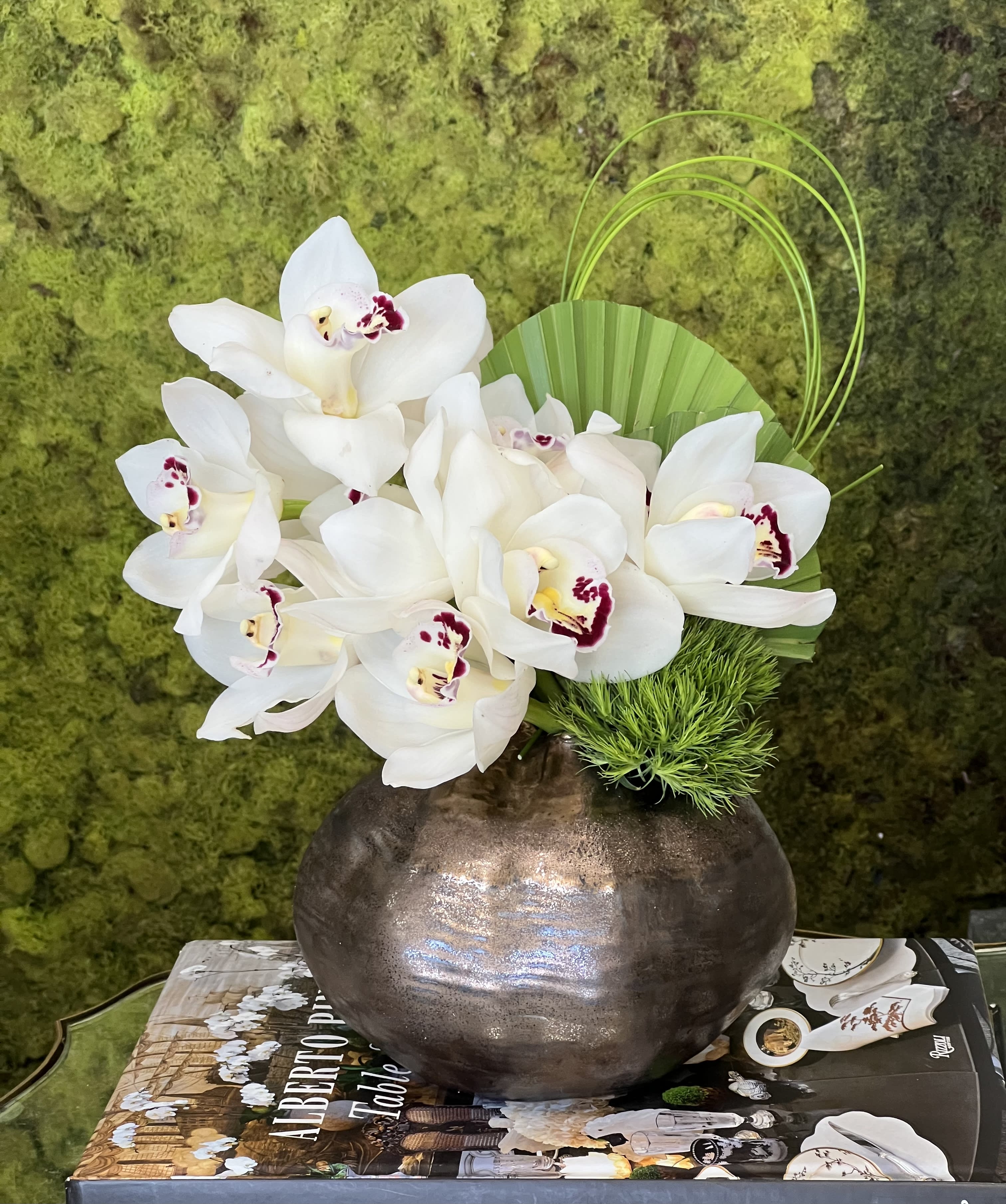 Rustic Orchid  - White Cymbidium Orchids, accented by select greens, in a metallic vase. The perfect size for a desktop or side table!