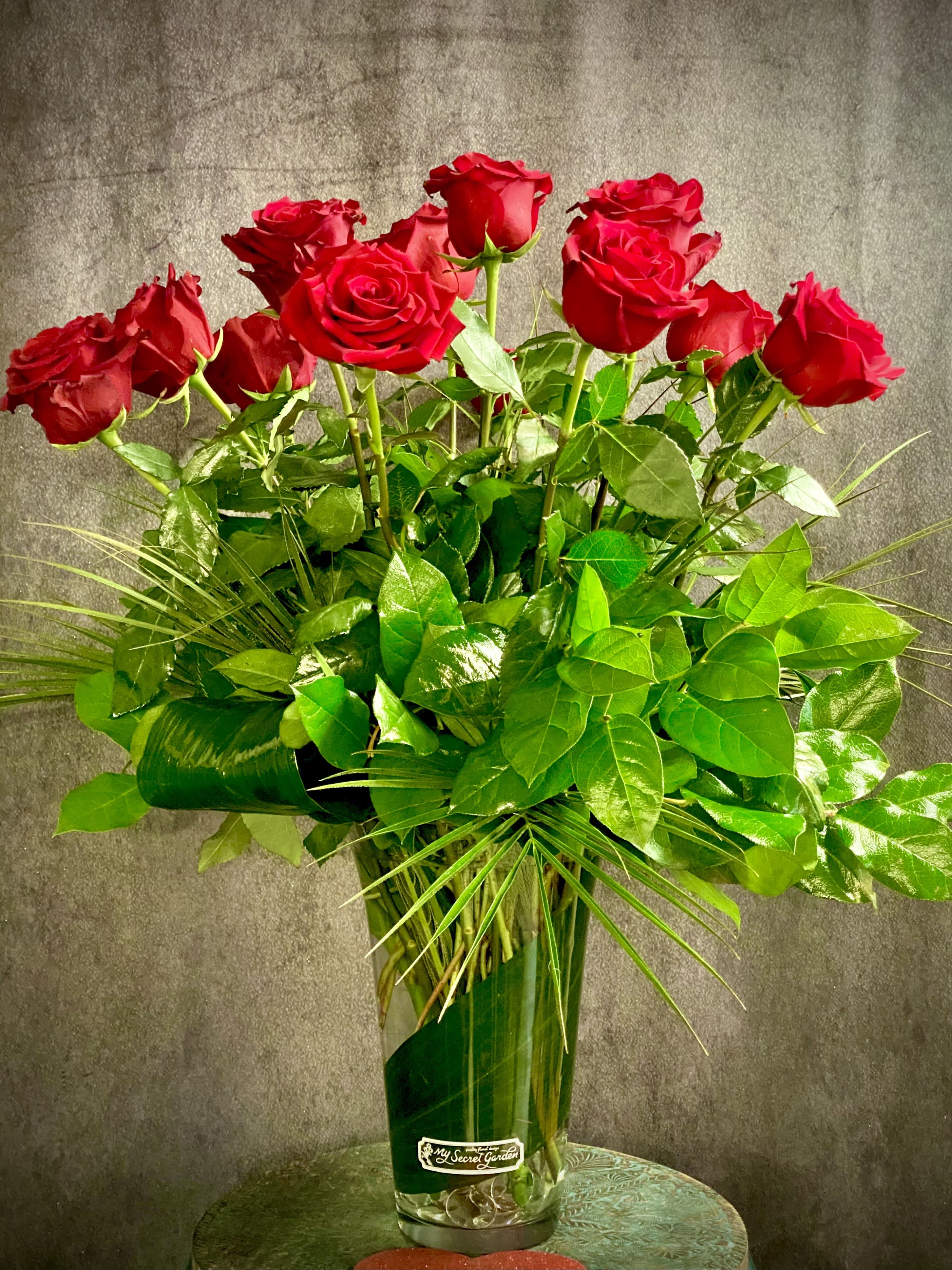 Valentine’s Grand Premium One Dozen Red Roses in Vase - One Dozen Premium Long Stem Red Roses arranged with tropical foliage in a clear glass vase.  Grand design that is a breathtaking presentation - sure to make your Valentine feel very special! Stands 35 inches tall.  