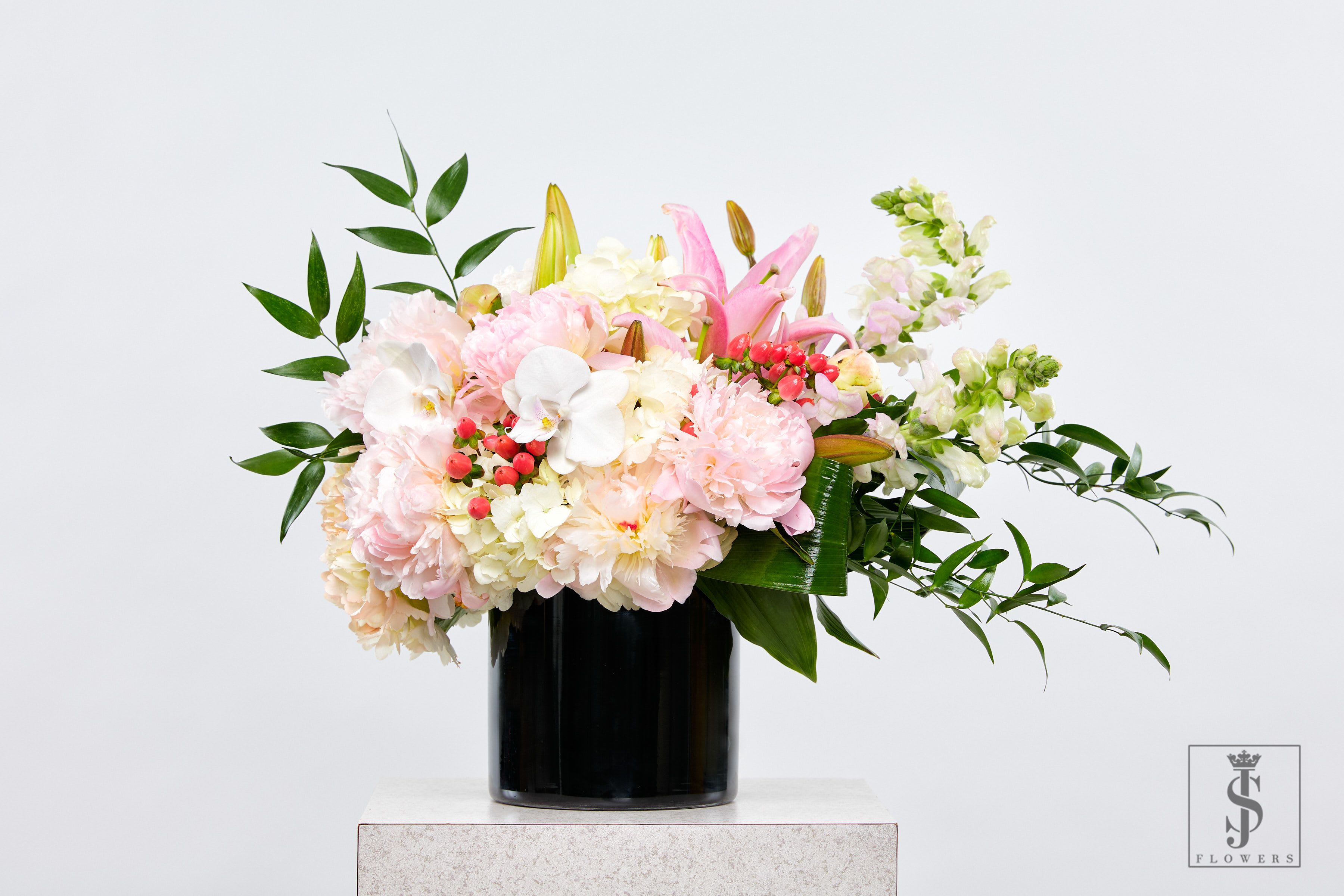 Pink Luxe - This delicate and luxurious floral arrangement features a dreamy mix of blush pink peonies, phalaenopsis orchids, lilies, snapdragons, and white hydrangeas, designed to capture soft elegance and timeless beauty. Accented with lush greens and red hypericum berries, this piece radiates romance and charm.  Arranged in a modern black cylinder vase, it’s the perfect floral choice for weddings, baby showers, anniversaries, sympathy gestures, or luxury décor. Now available for same-day delivery across the DFW metro — the perfect way to say "you’re loved" in full bloom.  