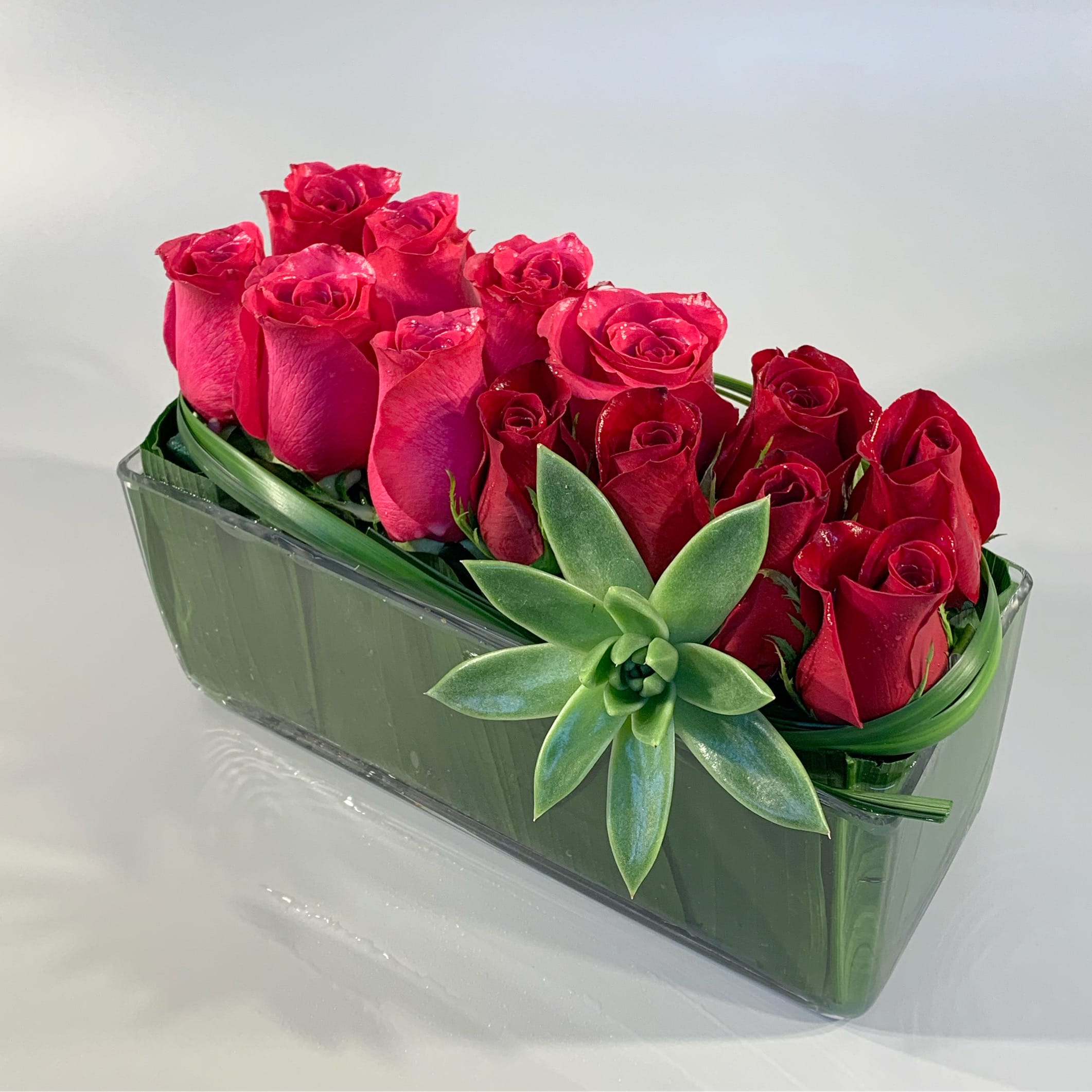 TOGETHER - A modern pave' of roses, accented with sculptural grasses, a succulent floret in a glass rectangular leaf-lined vessel. *Other roses colors may be used. Please specify in the special instructions box.