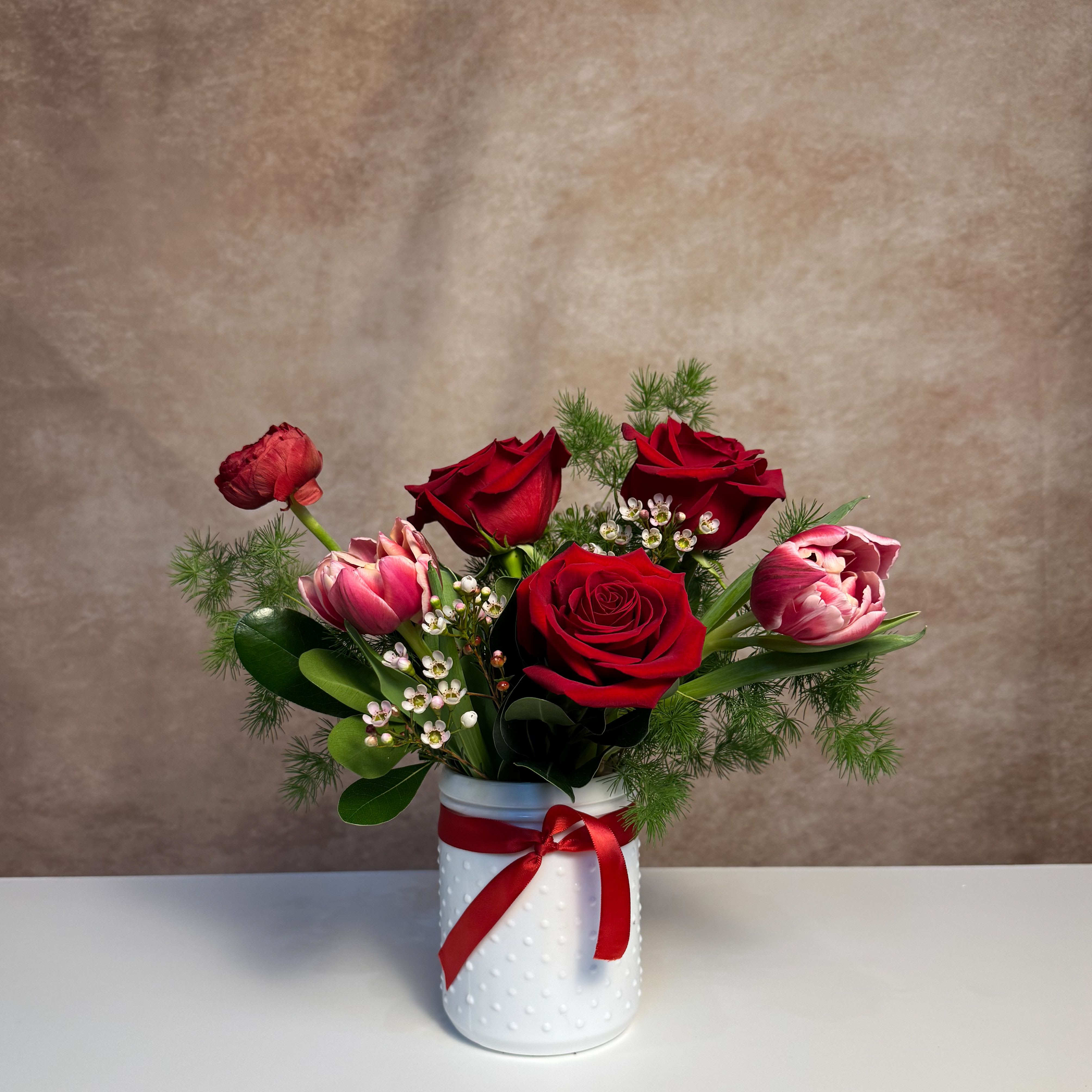 Crimson Crush - A classic red arrangement with red roses, tulips, and ranunculus in a white glass vessel. Measuring approximately 9x9, petite and perfect. Upgrade to deluxe for more roses and premium blooms.