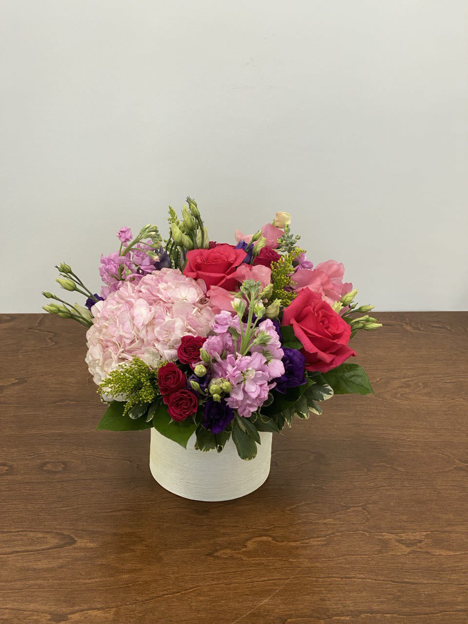 Pink Rhapsody - A captivating symphony of pink and purple blooms, featuring lush pink hydrangeas, elegant purple lisianthus, vibrant hot pink roses, charming spray roses, and fragrant pink stock. This bold and romantic arrangement is a celebration of color and beauty, perfect for making a statement on any special occasion. The container is a 5"x5" ceramic cylinder.