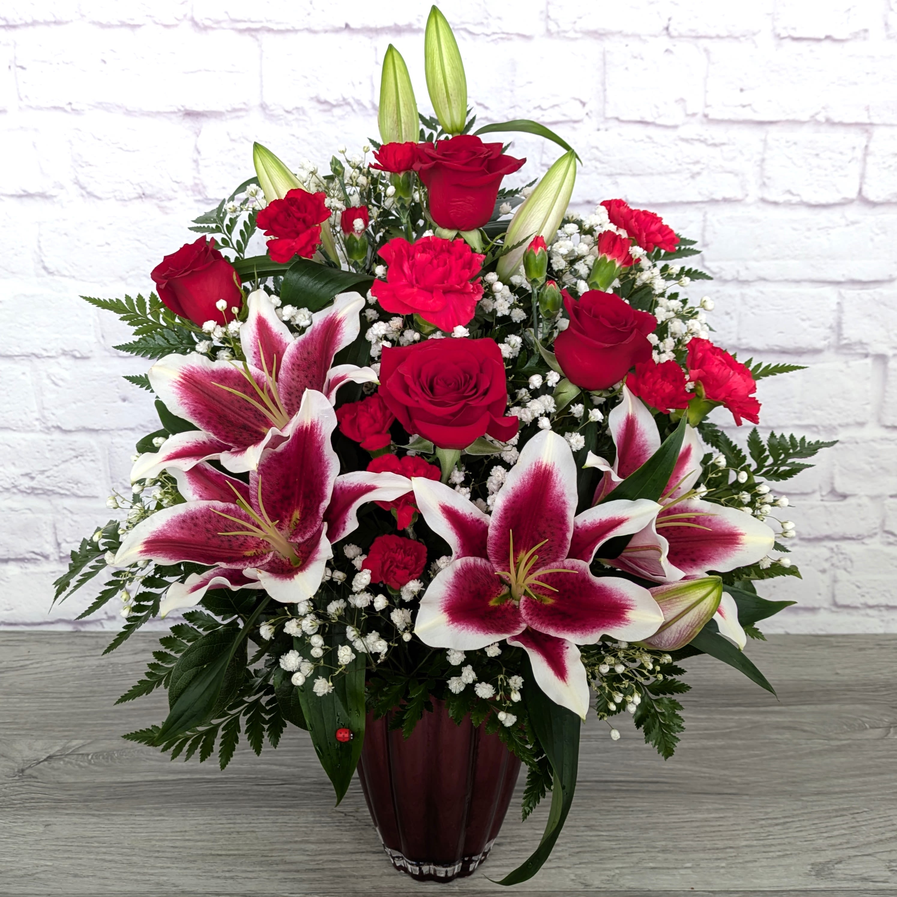 Berry Punch 2.0 - We are bringing back a Valentine's favorite from last year! Berry Punch 2.0! This bouquet features stargazer lilies, roses, carnations, mini carnations and babies breath. All in a scalloped red vase.  Orientation: One Sided 22” Tall 18” Wide   *Lilies may arrive in bud form, with proper care they will open up.* 