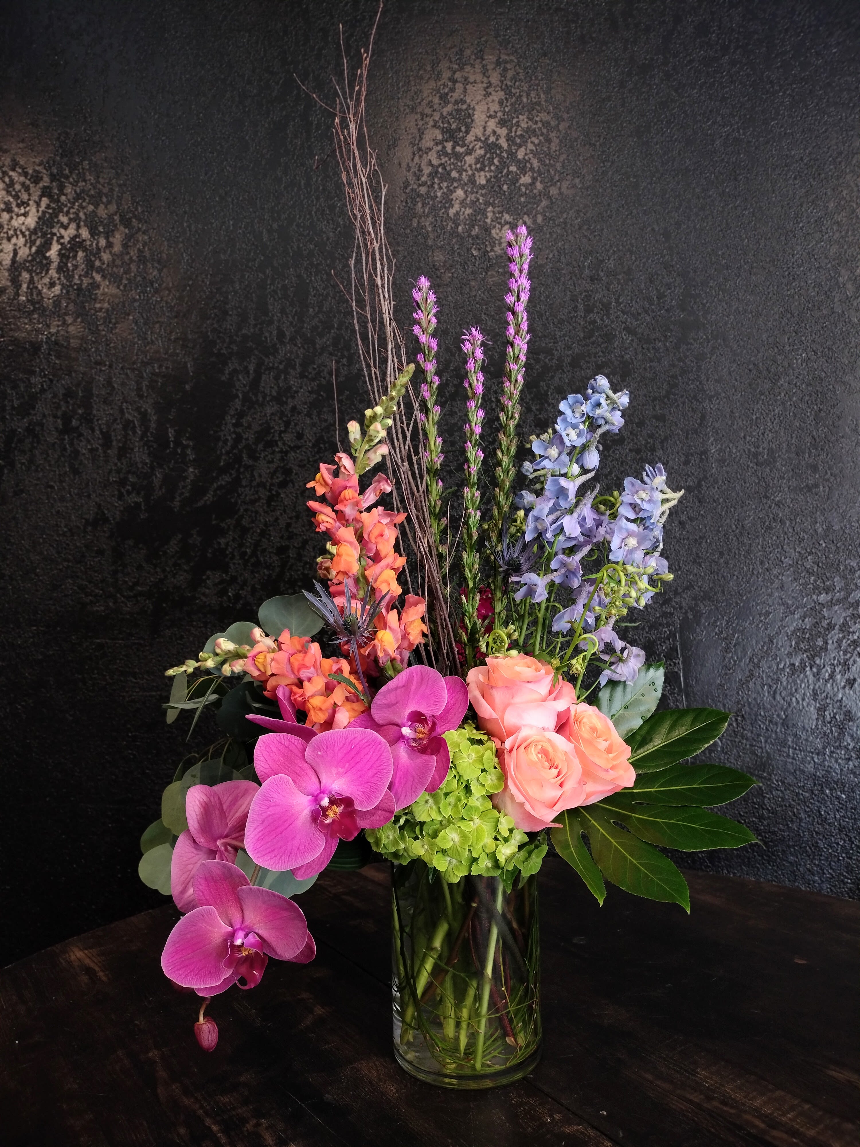 Dreamy Bloems - Dreamy Bloems has as many colors as a California sunset and is longer lasting! Give them a dreamy color palette in this new design.  Created in fun jewel tones with a half-dozen roses, cascading orchids, and flirty accent flowers.  Made in an 4x8" glass cylinder.