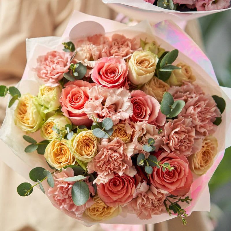 Vintage Allure - Presenting a mesmerizing hand-tied bouquet that exudes elegance and charm, perfect for any occasion. At the heart of this stunning arrangement are exquisite antique pink roses, their delicate, velvety petals showcasing a vintage allure that captivates the senses. Surrounding them, the soft blush carnations bring a touch of romantic whimsy, adding warmth and a playful spirit to the bouquet.  Delicately interspersed throughout are beautiful pink lisianthus blooms, renowned for their ruffled petals and graceful form, which create an enchanting texture and depth. Completing this harmonious composition are delightful peach spray roses, offering a sweet, sunny accent that elevates the overall palette with a hint of joy and brightness.  Adding a touch of nature’s freshness, fragrant eucalyptus lends its lush, muted green foliage, enhancing the bouquet’s romantic atmosphere while providing a soothing contrast to the pastel hues. Carefully hand-tied and wrapped in elegant, natural materials, this bouquet is a true work of art.  Perfect for celebrations, heartfelt gifts, or simply to brighten someone's day, this hand-tied bouquet embodies beauty and sophistication. It’s more than just flowers; it’s a heartfelt expression of love and appreciation that will bring joy and smiles to anyone who receives it.