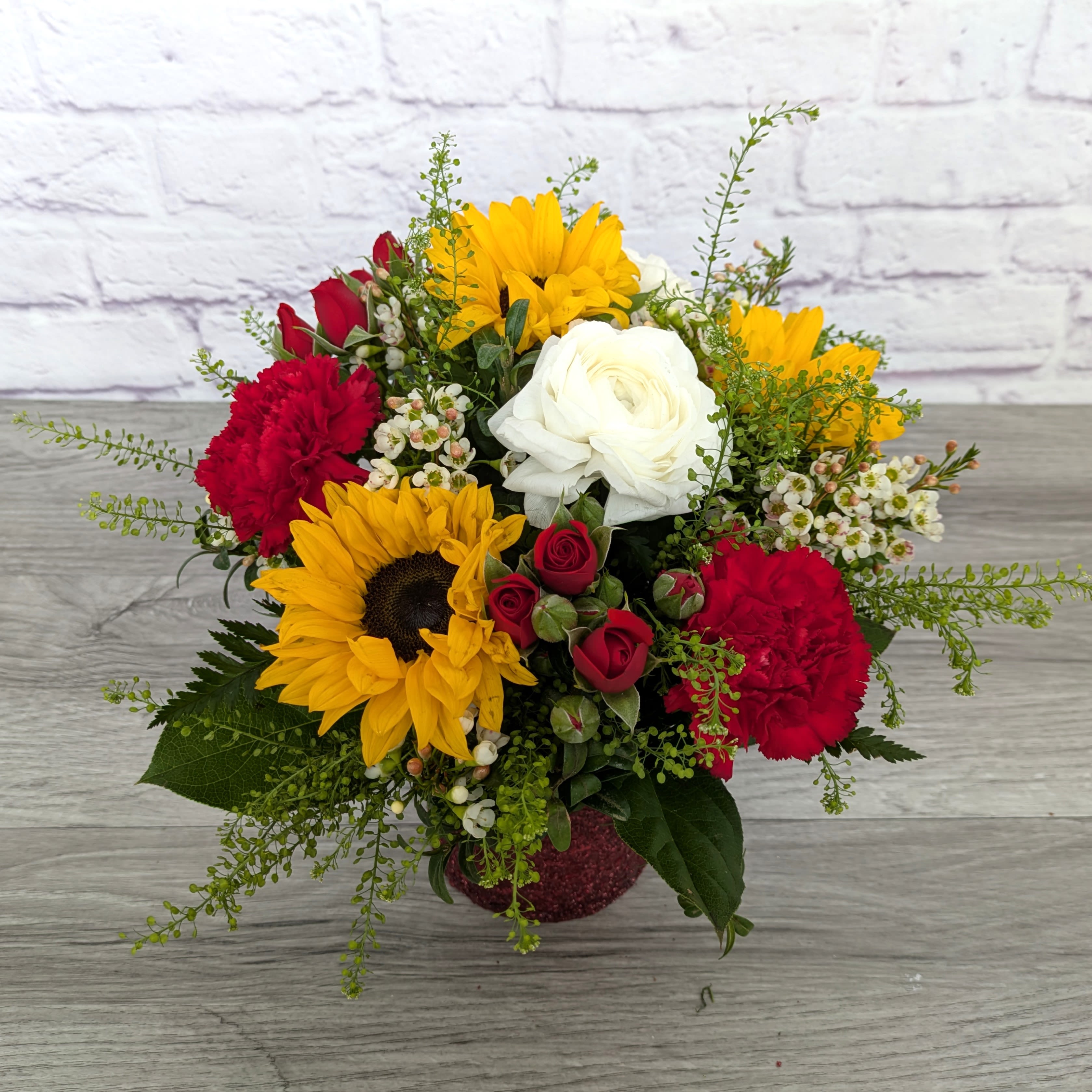 Sunshine and Roses - Sunshine and Roses is A Ladybug Floral Exclusive bouquet.  This bouquet features sunflowers, ranunculus, spray roses, carnations, wax flower and penny cress in a 4.5” cylinder with textured and shimmering finish.  Orientation: All Around 12” Tall 12” Wide  
