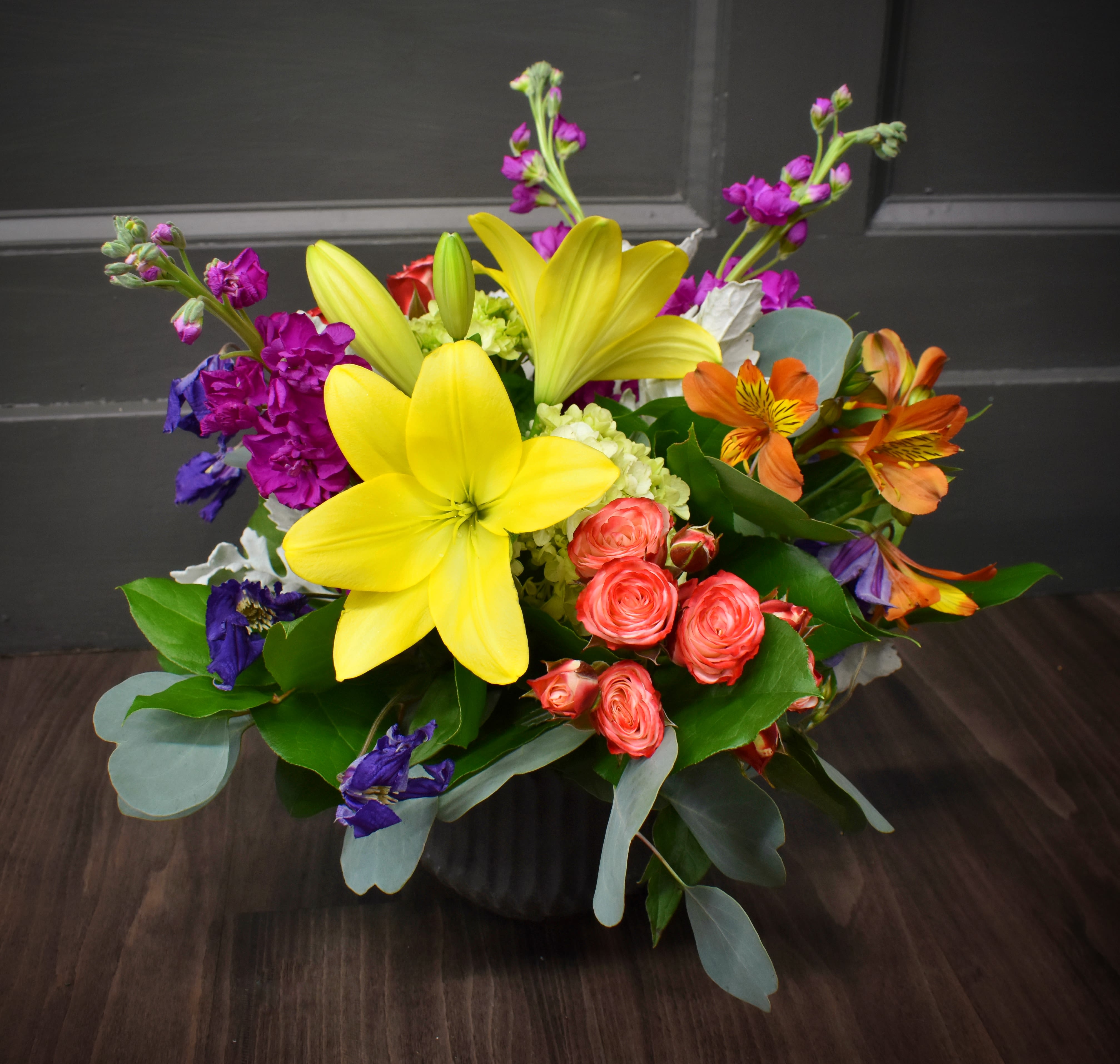 Color Burst - Available for local St Cloud, MN area delivery only - A brightly colored centerpiece designed with lilies, alstromeria, spray roses and more! This design comes delivered in a textured pottery container, nice for a keepsake. Approx. 12"h x 14"w