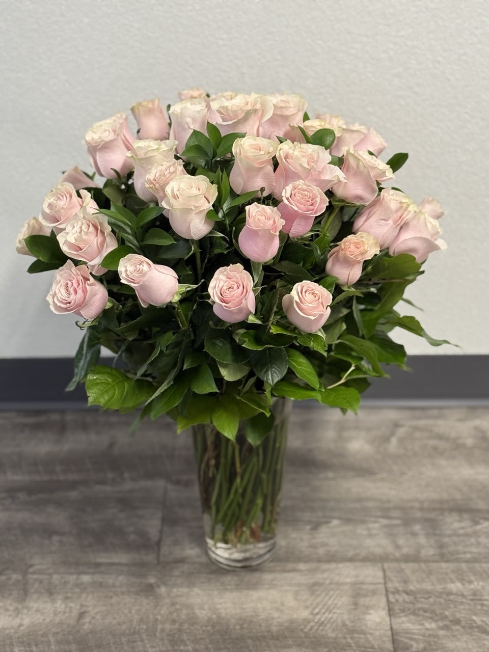 3 Dozen Light Pink Roses - A joyful gesture of love and affection, this chic arrangement of light pink roses with fresh greens is a special surprise on any occasion. The light pink roses are arranged with salal and delivered in a clear vase.