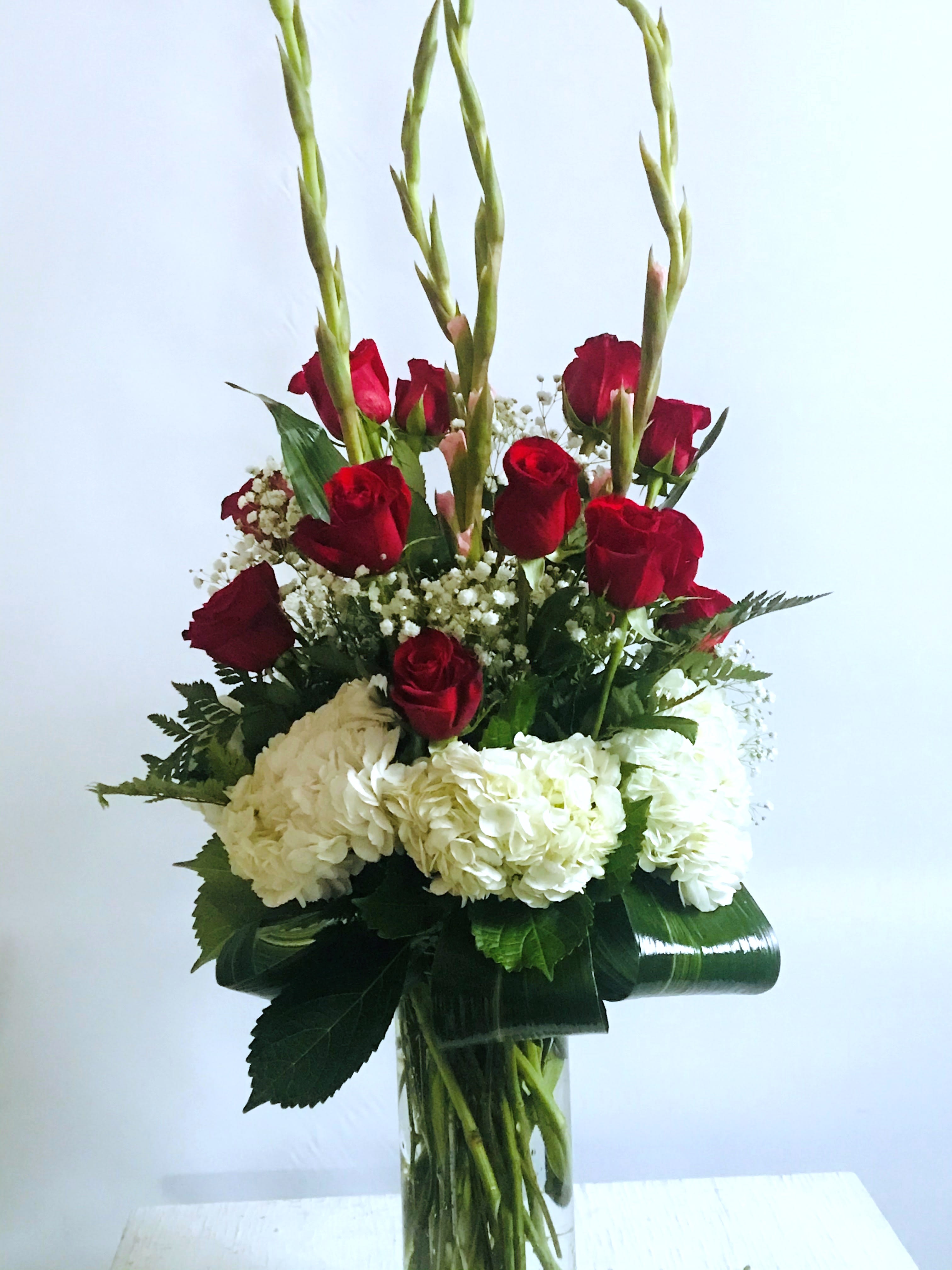 Anniversary #14 - An arrangement of fresh cut roses, hydrangeas and gladiolas designed in a tall clear cylinder vase. Embellished with folded Aspidistra leaves