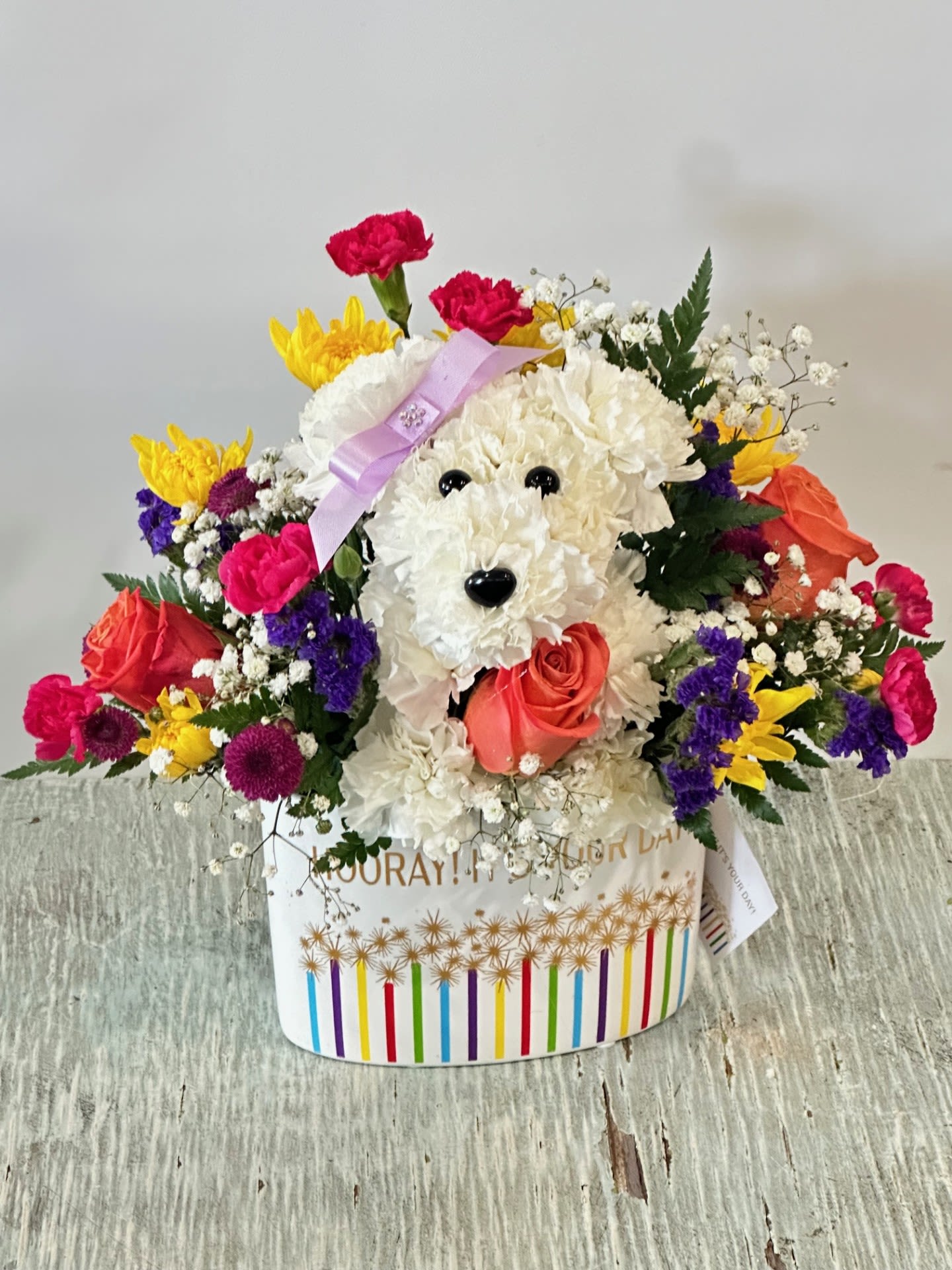 Birthday #11 - Arrangement of fresh cut flowers that includes a puppy made out of carnations in a “Hooray! It’s Your Day!” keepsake container adorned with colorful sparklers topped with metallic bursts of light; measures 5"H x 8.6"L x 4.25"W. Colors can be modified depending on availability.
