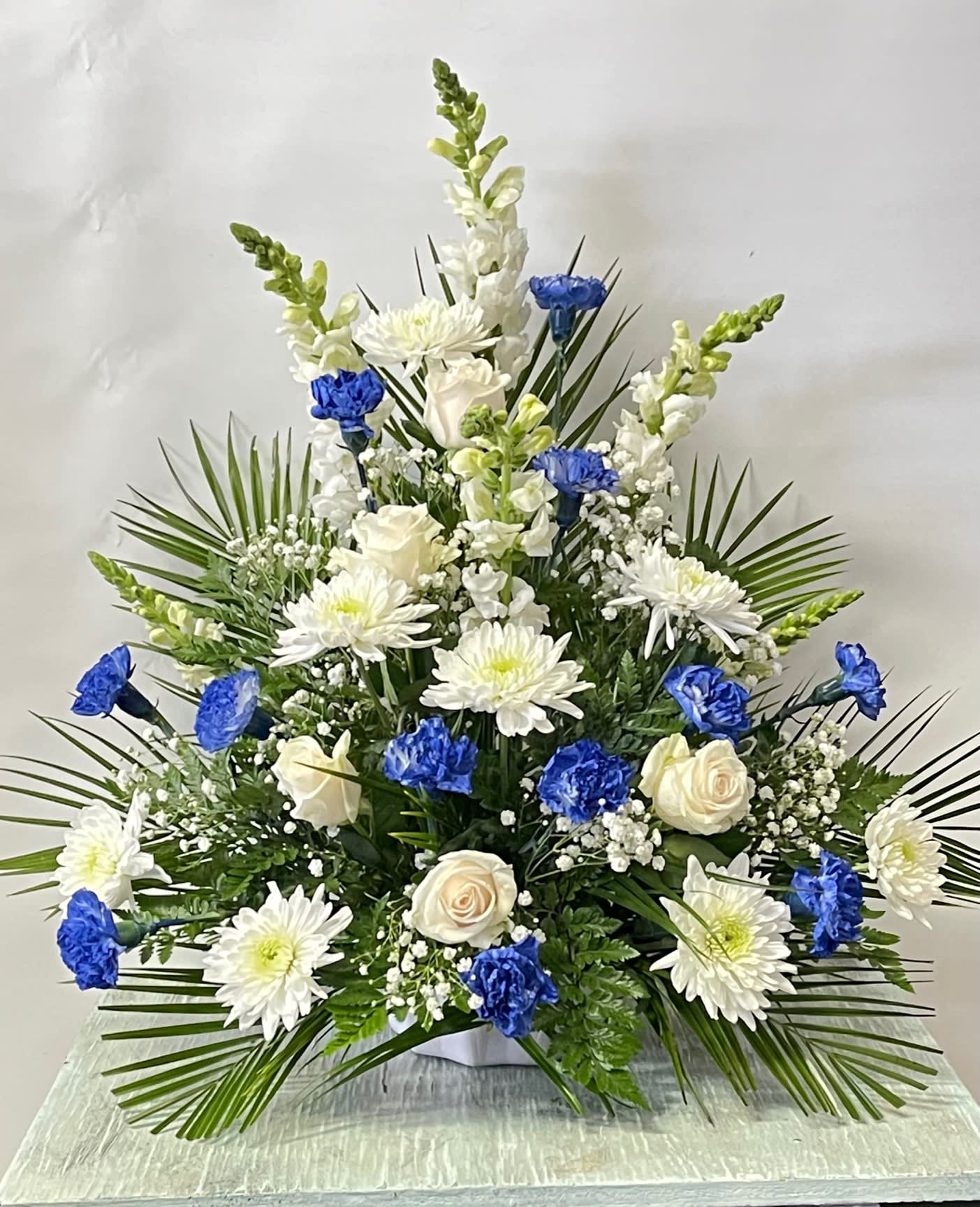 Sympathy #7 - Sympathy arrangement of white and blue flowers. Carnations naturally do not come in blue. They are either dyed or spray painted depending on demand. Color can be modified depending on availability.