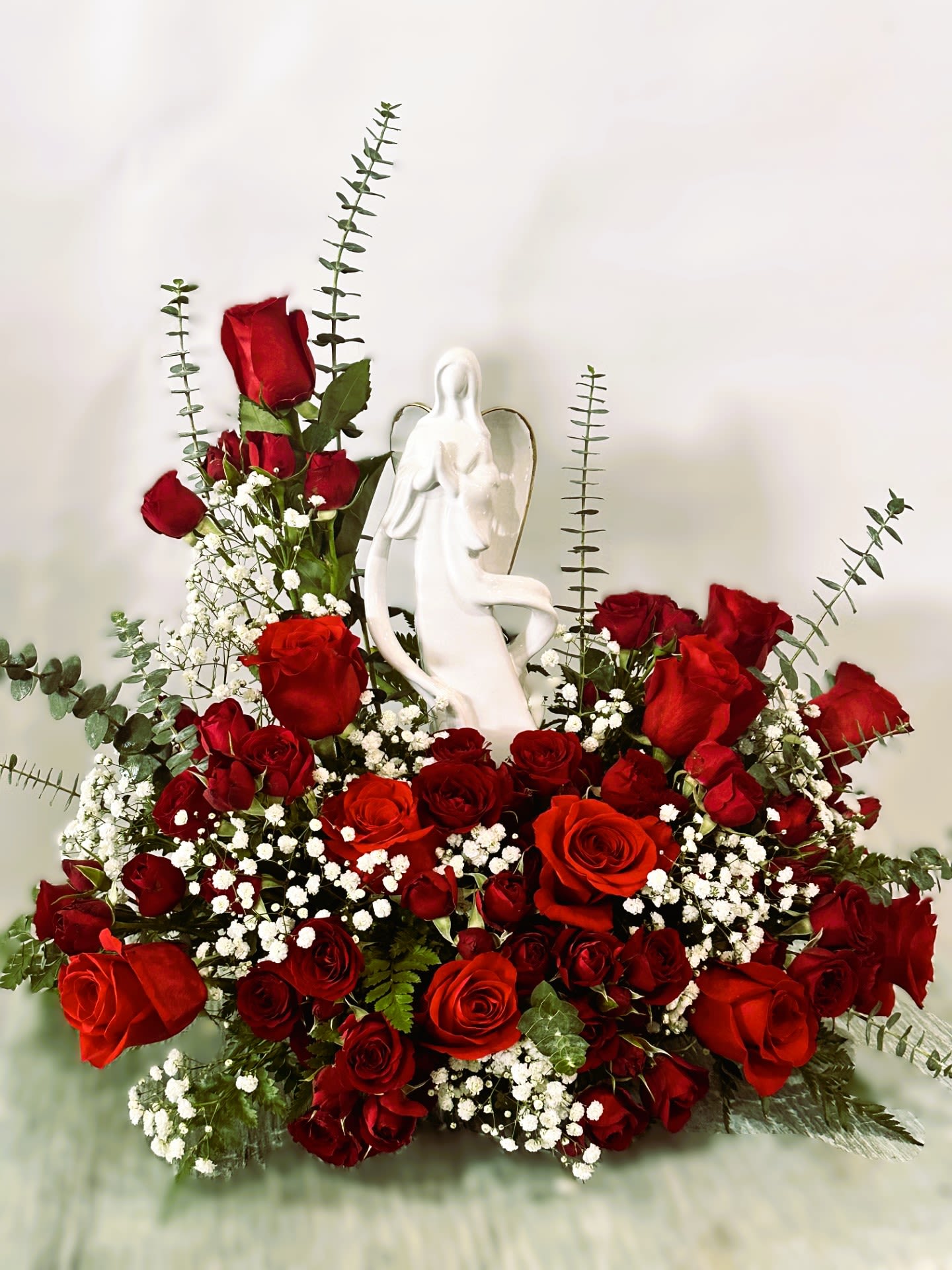 Sympathy Statue Arrangement #12 - Sympathy arrangement of all red roses with a touch of babies breath and eucalyptus surrounding an all white angel statue.