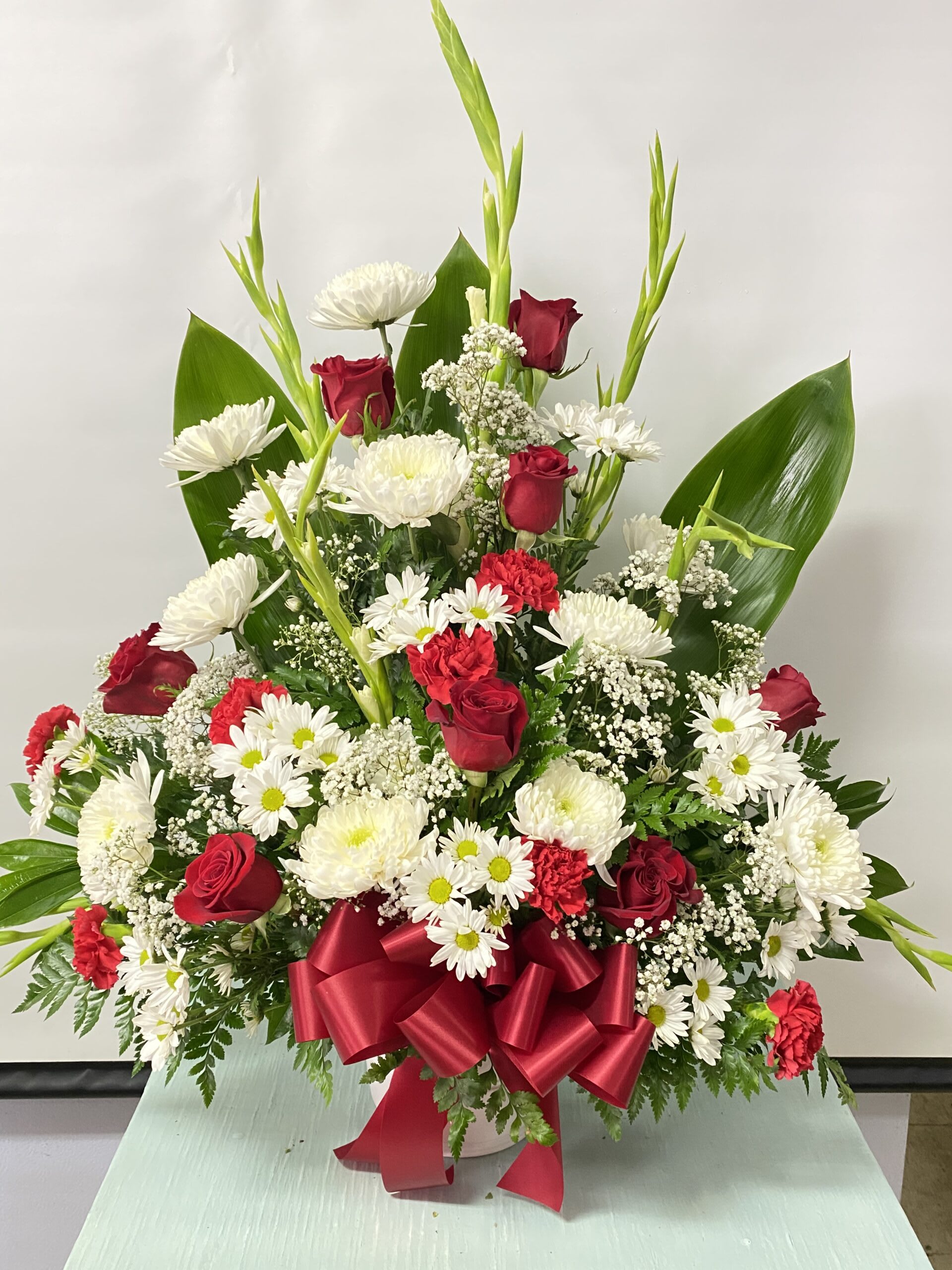 Sympathy #24 - Sympathy arrangement of fresh cut flowers designed in a paper mache container. Arrangement pictured in white and red. Colors can be modified depending on availability.