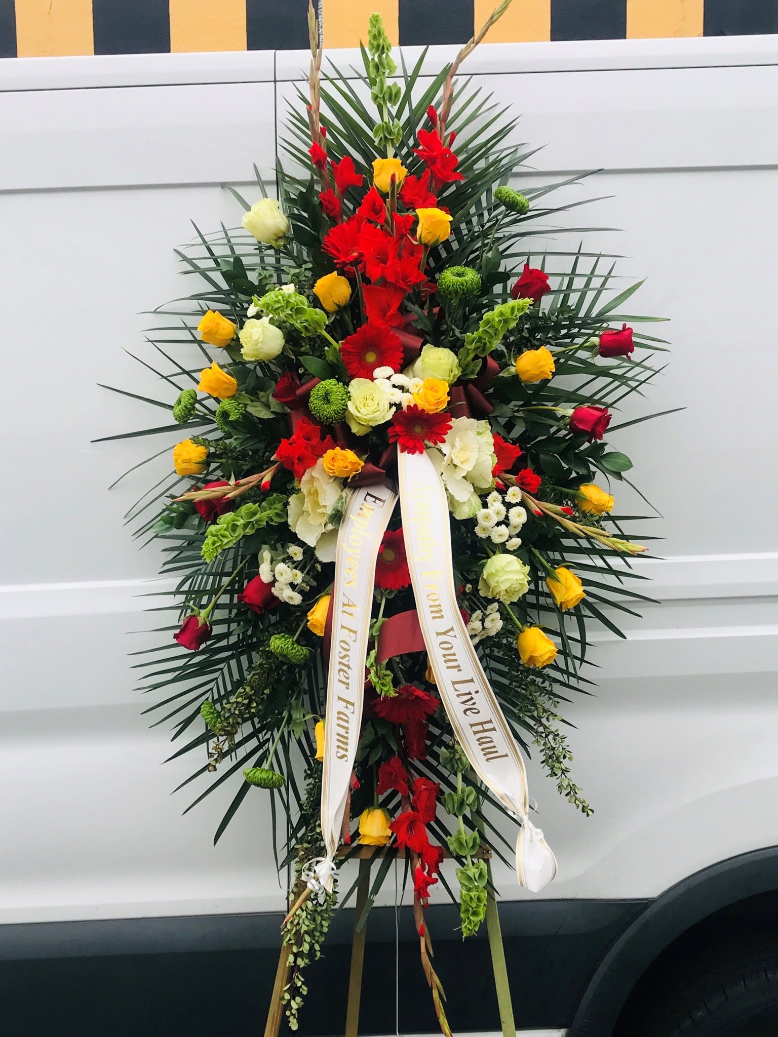 Sympathy Standing Spray #40 - Standing spray of red, green and yellow fresh cut flowers. Colors can be modified depending on availability. Designed on an easel that is included with arrangement and does NOT need to be returned. Banners are included with arrangement. Please specify what is to be printed on each banner upon check out under "FLORIST INSTRUCTIONS". LIMITED TO 5 WORDS PER BANNER.