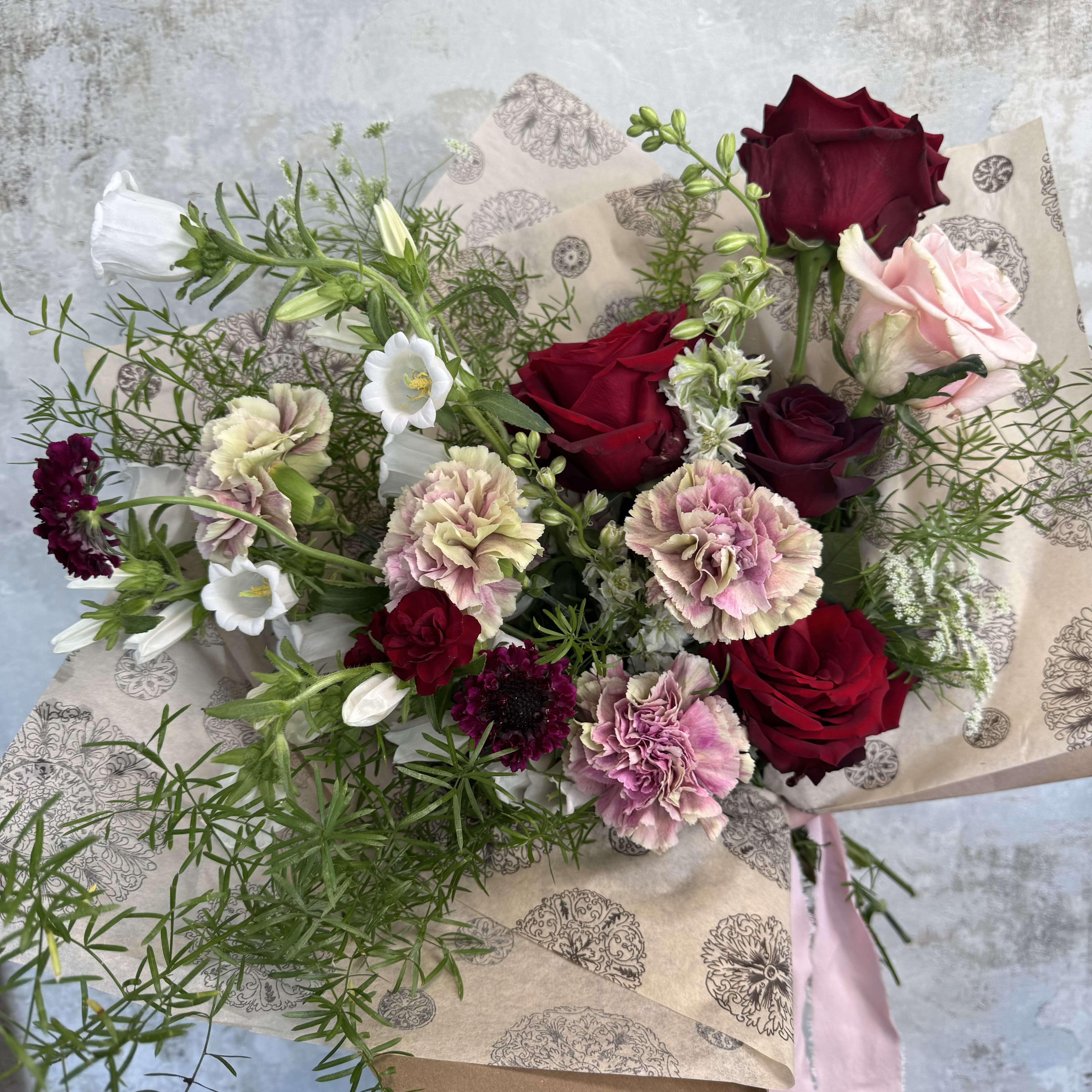 (Valentine's Day) I Adore You Bouquet - A heartfelt expression of love, admiration, and affection, the "I Adore You" bouquet brings together the timeless romance of reds, pinks, and whites in a beautifully hand-tied wrap. This thoughtful gathering of seasonal blooms and delicate accents is designed to speak volumes.  Deep red flowers convey passionate love, soft pinks offer gentle admiration, and pure whites evoke the beauty of a fresh start or a sincere connection. Perfect for anniversaries, meaningful milestones, or simply as a tender reminder of how much someone means to you, this bouquet captures emotion in every petal.  Each bouquet is artfully wrapped in our signature style and finished with raffia (ribbon substitution available)—ready to present as a meaningful gift. Depending on the size selected, the quantity and variety of flowers will vary to best suit your chosen style.  For a personalized touch, feel free to include any special notes or requests at checkout—we’d be honored to make your bouquet uniquely special.