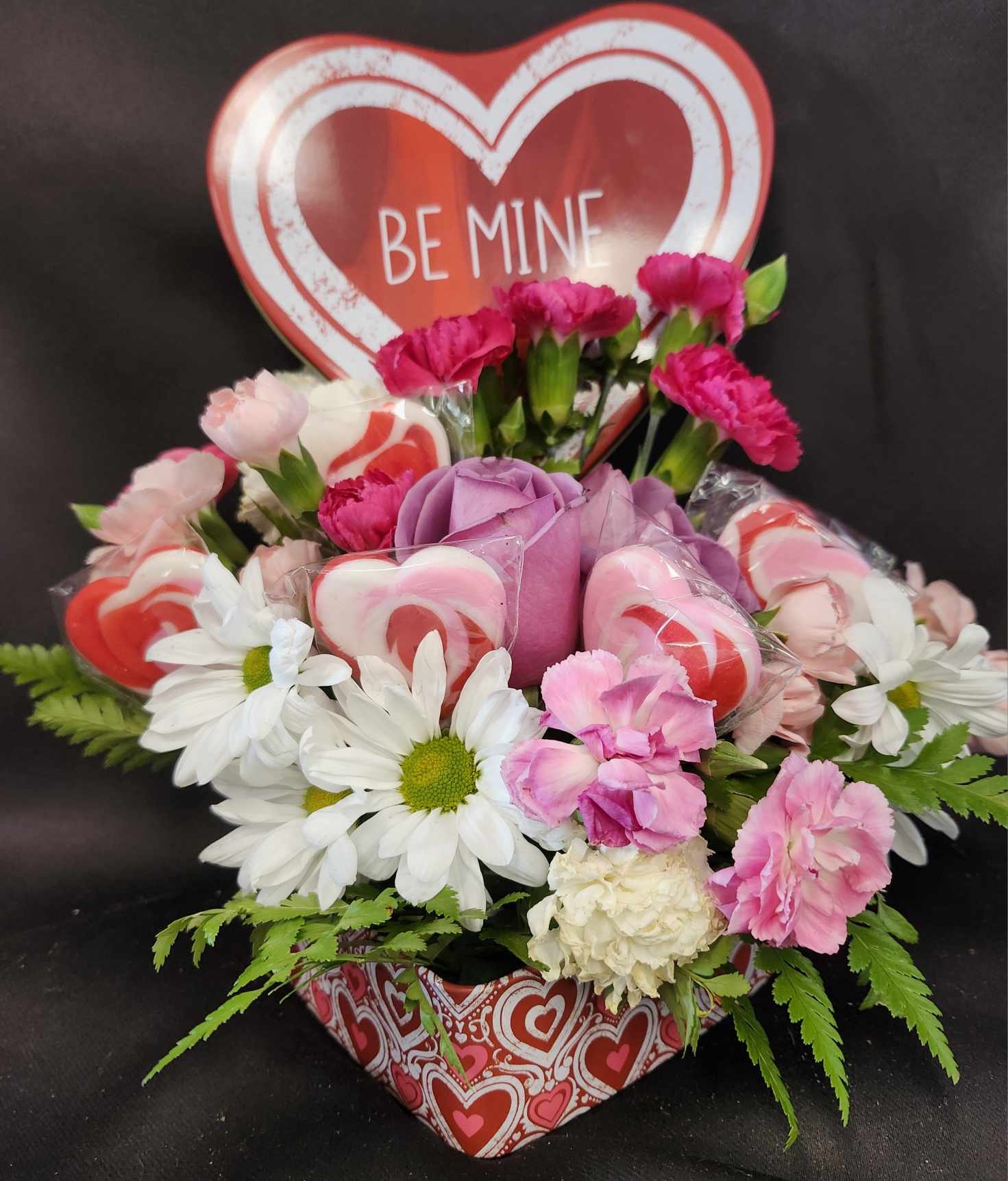 Sweets For Your Sweetheart - In a keepsake heart shaped tin this pretty arrangement holds spray roses and carnations with seasonal greenery and 6 sweet suckers.