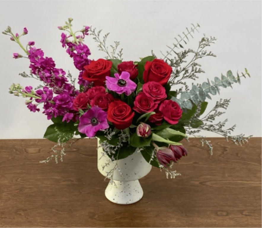 Wild at Heart - Fuchsias and reds come together to make a beautiful display of roses, spray roses, stockflower, tulips, and anemone. Elegantly designed in a modern white speckled compote.