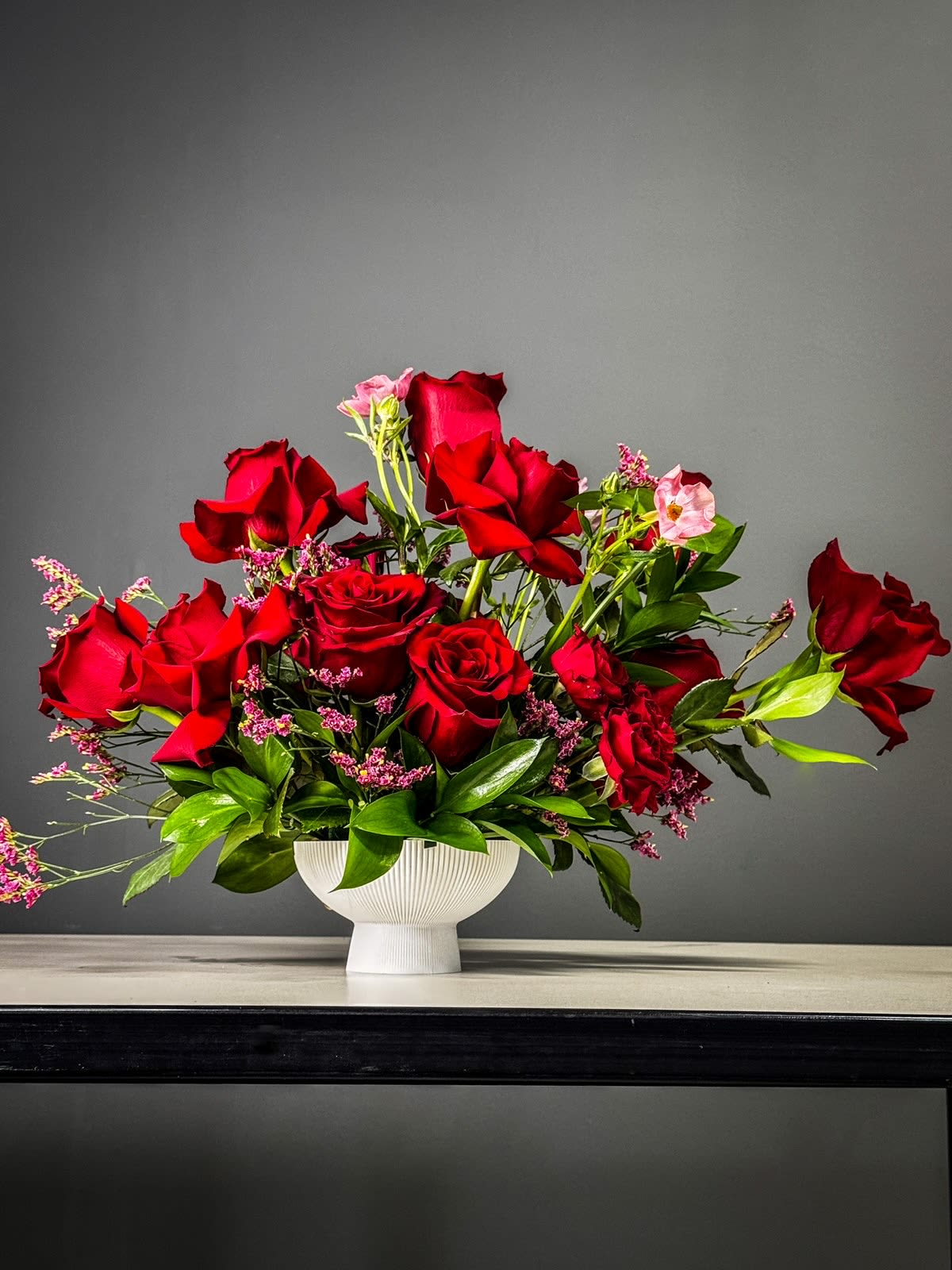 Eternal Beauty - The "Eternal Beauty" flower centerpiece is a captivating arrangement that exudes timeless elegance and charm. Featuring a harmonious blend of rich red roses and delicate spray roses beautifully displayed in a ribbed pedestal bowl, this centerpiece is a stunning focal point that evokes a sense of everlasting beauty and grace. The deep crimson hues of the roses contrast with the soft petals of the spray roses, creating a lush and romantic composition that is sure to impress and enchant any setting with its sophisticated allure.