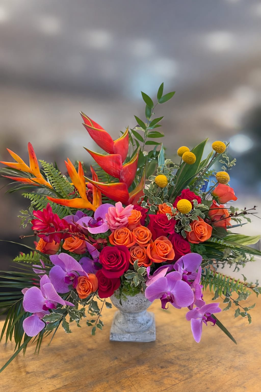 Vintage Sunrise - Flowers: orange roses, pink roses, billy balls, purple phalaenopsis orchids, ginger, italian ruscus, sword fern, palm leaves, and greenery.  Vase: medium stone compote vase