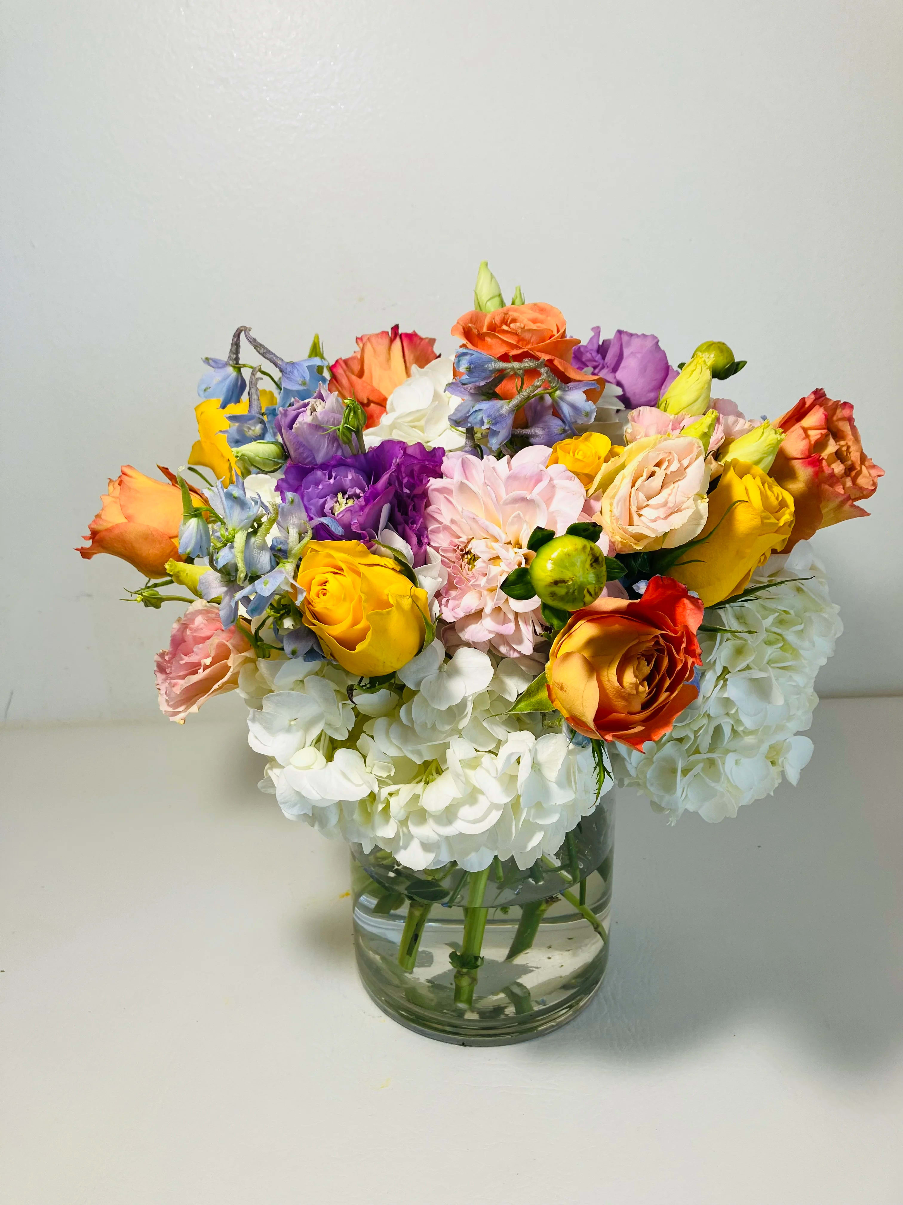 Spring Garden - Spring Garden: Spring Garden were integral elements of farming culture, where jams and pickles were judged and awarded prizes at fairs and festivals. In these contests, color and beauty were often scored as day turned to night with kids chasing fireflies and lining up for fun rides.This vintage design would be a winner with a younger yet old-fashioned feel. Main colors: white, orange, yellow, Lila. Typically includes: Orange Roses, Bupleurum, Alstroemeria, Green Buttons. Subject to substitution.