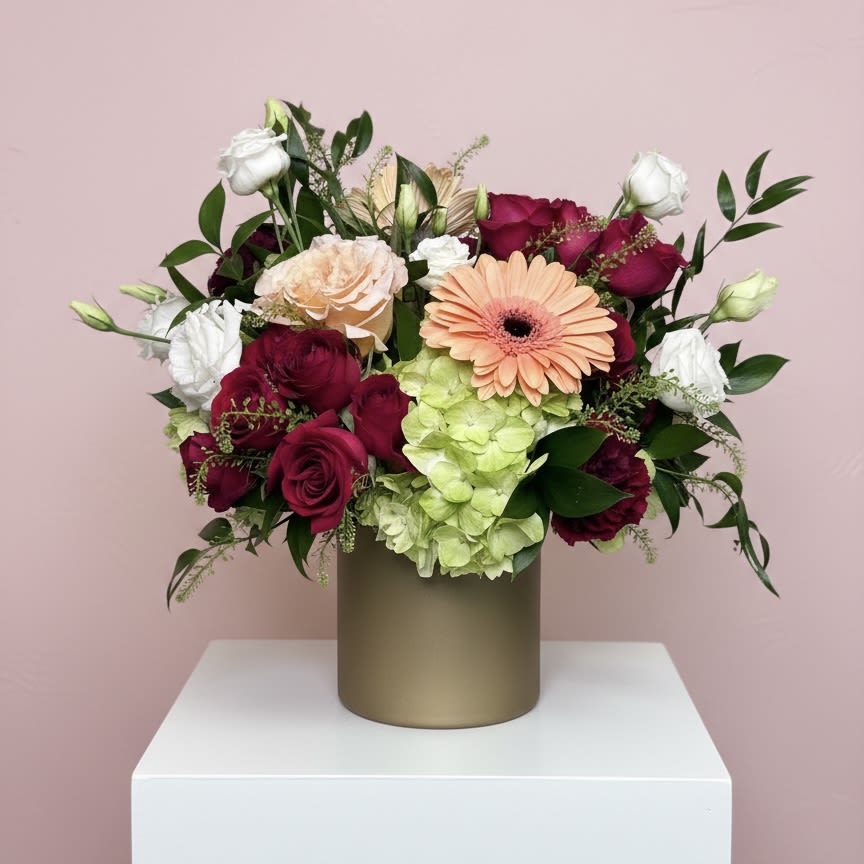 Golden Amor - Lush burgundy and peach blooms featuring roses, hydrangea, spray roses, gerbera daisy, lisianthus and carnations in a 5'' gold cylinder