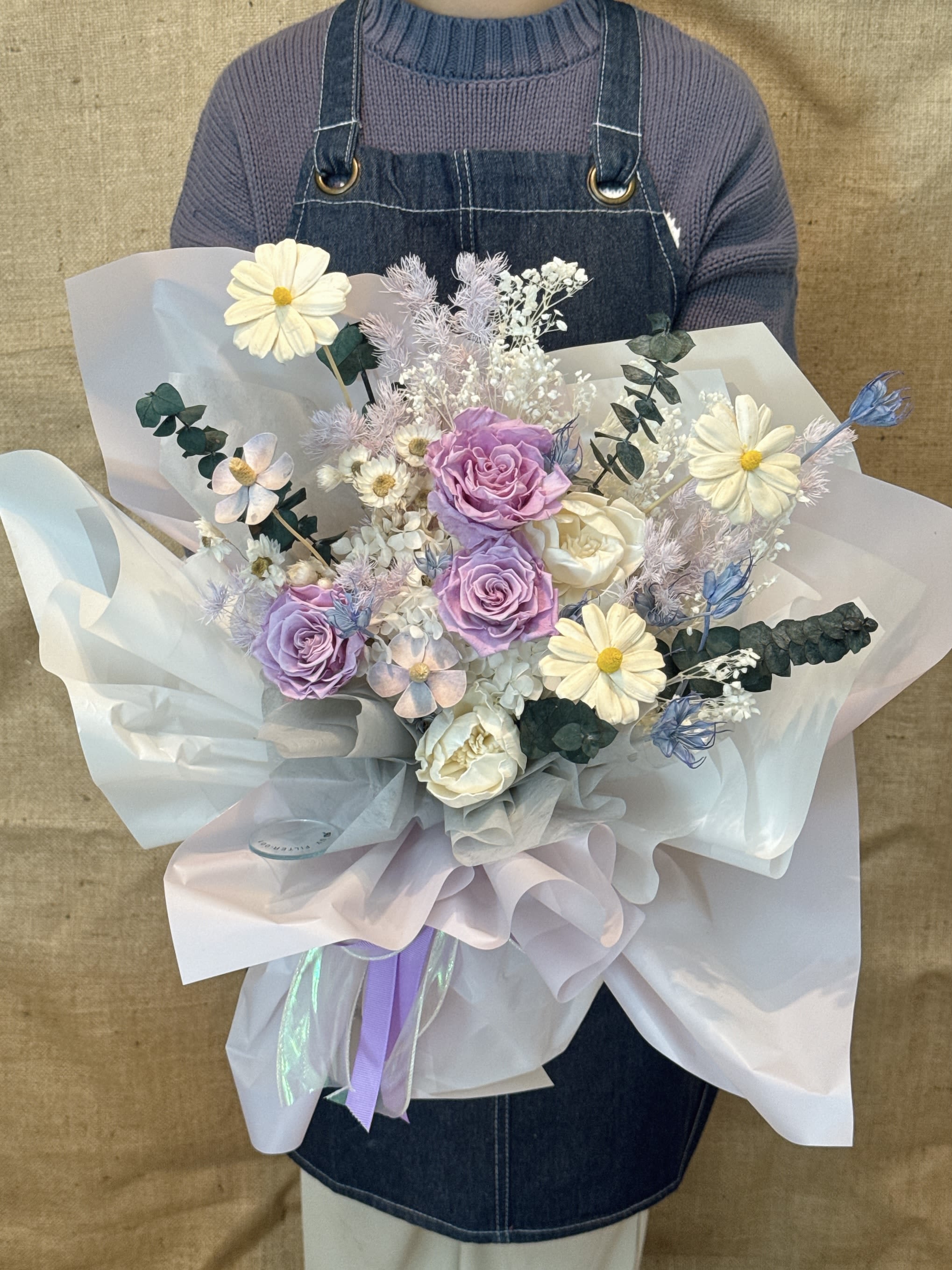 Soft Embrace - This is a Korean ins-style mix-and-match bouquet. Its color matching is low-key and noble, giving people a romantic, elegant and dreamy feeling. Flower materials and color matching The bouquet is mainly in soft purple and white tones: Main flower: contains many purple roses, symbolizing tenderness and persistence. Matching flowers: with small white daisies (or chamomile), representing innocence, hope and deep love. Decoration: A little light blue flowers, eucalyptus leaves and other ingredients are used to add a sense of hierarchy and fresh and natural style. Style and packaging The bouquet adopts the popular Korean style packaging: Wrapping paper: White and light purple transparent tulle or organza are wrapped in layers to create a light and fluffy "fairy" effect. Design: The overall design pursues a casual, natural, exquisite and simple feeling, which is very suitable for taking photos, and it looks good no matter how you take it. Meaning and use This bouquet combines the love of roses and the innocence of daisies, implying beautiful and pure feelings. Occasion: Suitable for birthday gifts, anniversaries, Valentine's Day, graduation gifts or any occasions that need to create romantic surprises. Object: It is especially suitable for giving to beloved partners or important female relatives and friends (such as mothers) to express special care and gratitude. 