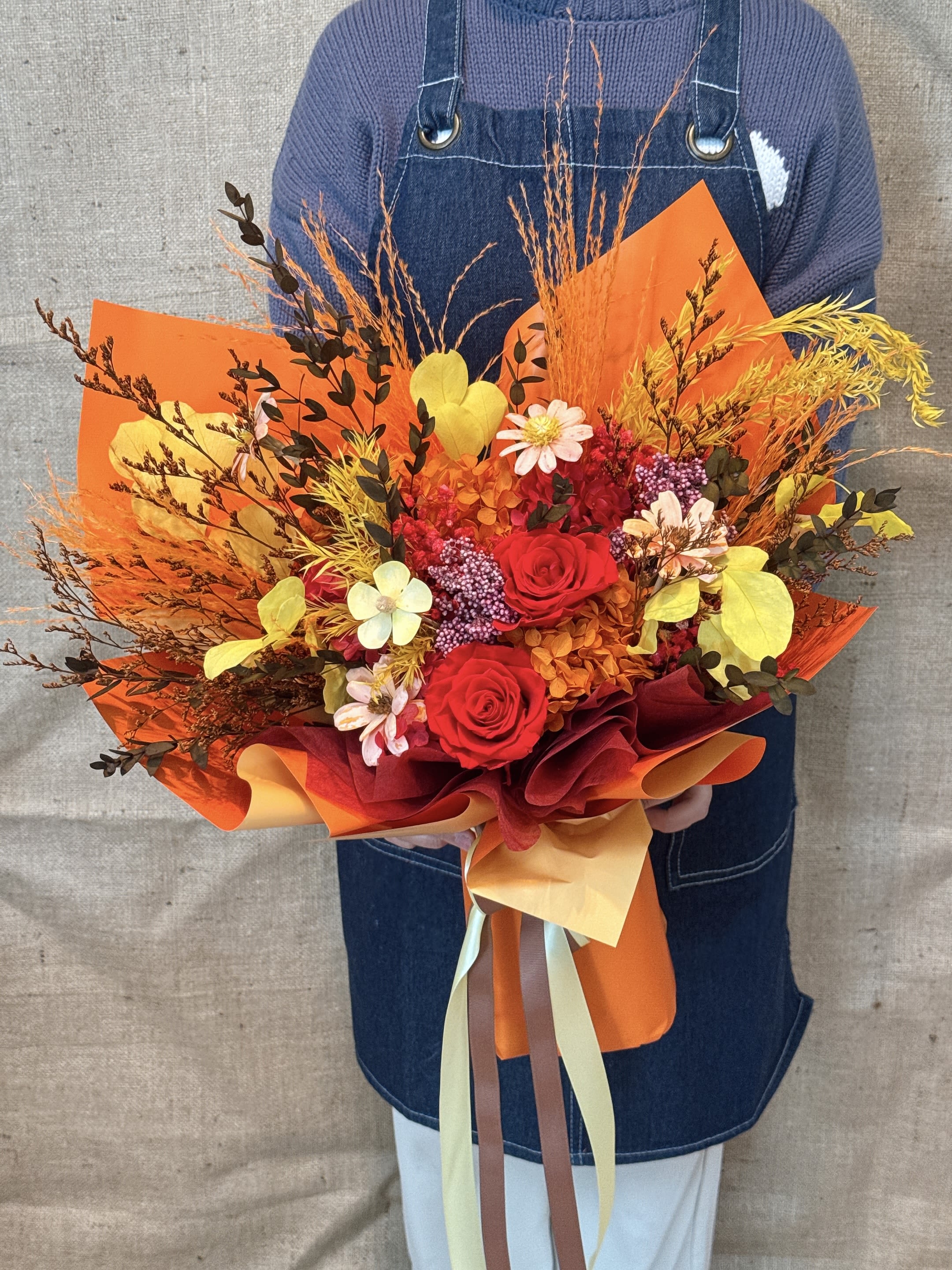 Bright Moments - This is an exquisite orange-red bouquet. The main color is warm and strong, which is very suitable for expressing warm love. Tone The bouquet combines orange, yellow and red flowers, with dark brown or black leaves and light-colored wrapping paper, presenting a warm and atmospheric tone as a whole, giving people a warm and energetic visual feeling. Flower materials The main flower materials include immortal roses, small daisies, orange gerberas, full stars, and dried flower materials such as golden hammer flowers and mangroves. Meaning Orange bouquets usually symbolize enthusiasm, luck and warmth. Red roses represent passionate love, and yellow flowers bring sunshine and hope. The whole implies long-term and unchanging love and protection. Occasion This bouquet is very suitable as a birthday gift, anniversary, Valentine's Day gift or marriage proposal bouquet, at special moments when you need to express sincere and strong emotions.