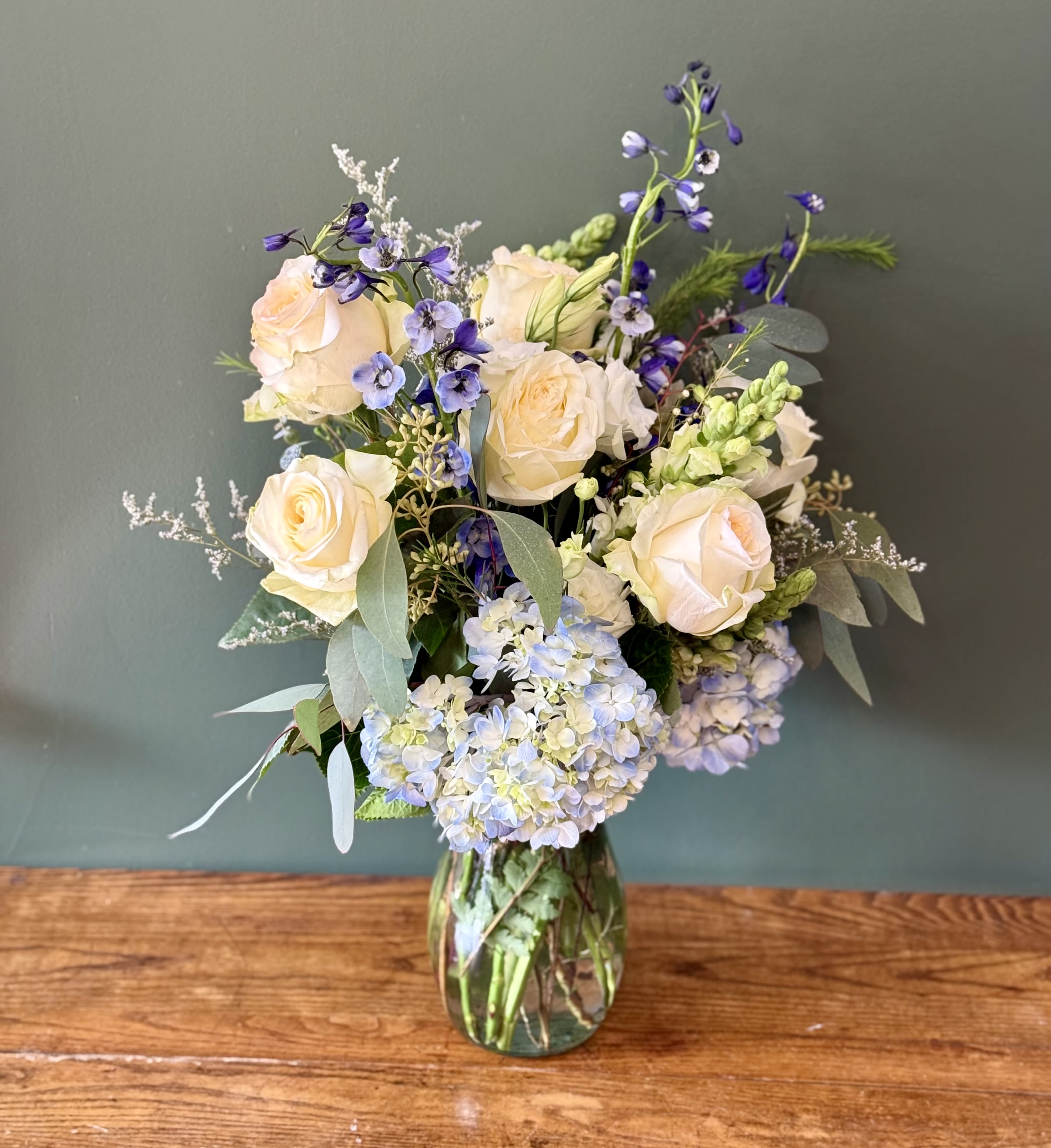 Timeless White and Blue - This elegant white and blue floral arrangement features fresh white and blue flowers thoughtfully designed for a timeless look. A versatile choice for many different occasions. Featuring: - Ecuadorian Roses - Hydrangeas - Delphinium - Stock - Styled with premium seasonal foliage  Presentation Options: Tall clear vase measures approximately 9" in H. Vase included in price. Every order includes: A custom message card - simply enter your message at checkout and we'll take care of the rest. As a local florist in Charleston South Carolina, everything is made fresh by us here at our flower shop Downtown Charleston.  Please note: Flowers are subject to seasonal availability. If a listed flower is unavailable, our designers will substitute it with flowers of a similar shape, color, and style to maintain the overall aesthetic.
