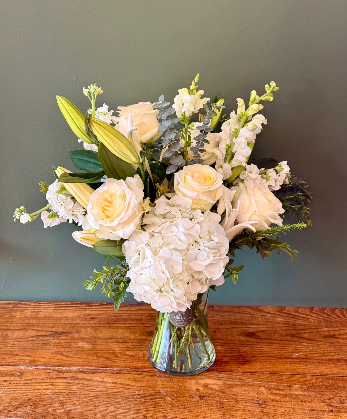 Pure White  - The Pure White floral arrangement features a timeless blend of fresh flowers, beautifully designed to convey elegance, peace, and simplicity. This all-white flower arrangement is perfect for any occasion that calls for a graceful touch. Featuring: - Ecuadorian Roses - Asiatic Lilies - Snapdragons - Stock - Hydrangeas - Styled with premium seasonal foliage Presentation Options: Clear tall vase measuring approximately 9" H. Vase included in price. Every order includes: A custom message card - simply enter your message at checkout and we'll take care of the rest. As a local florist in Charleston South Carolina, everything is made fresh by us here at our flower shop Downtown Charleston.  Please note: Flowers are subject to seasonal availability. If a listed flower is unavailable, our designers will substitute it with flowers of a similar shape, color, and style to maintain the overall aesthetic.
