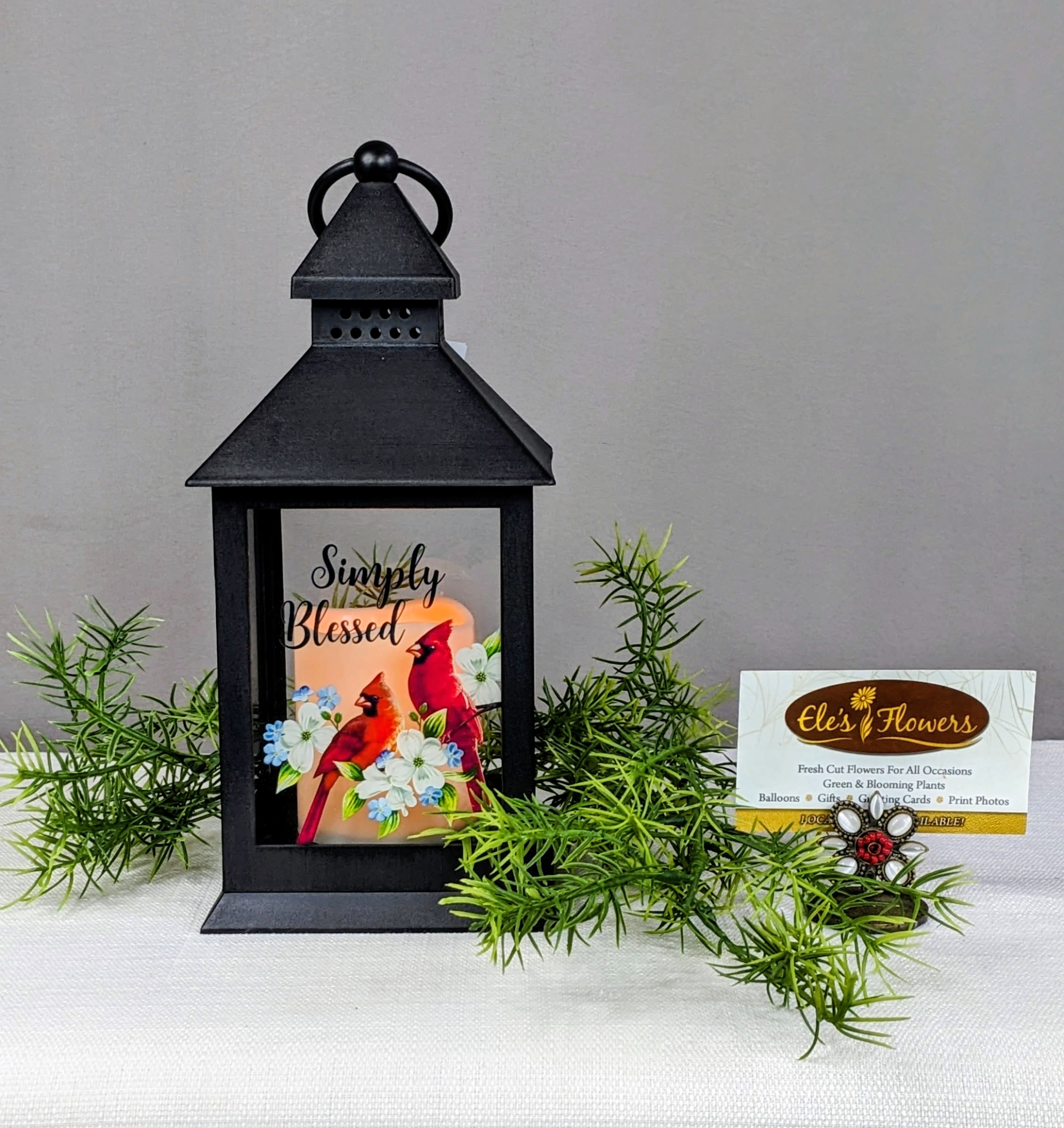 Simply Blessed - Lantern  - A keepsake lantern with an LED flicker candle is a thoughtful memorial piece designed to provide comfort and remembrance. Made from durable plastic, the lantern features a timeless design with clear panels that allow the gentle, realistic flicker of an LED candle to shine through. This lantern serves as a lasting tribute, offering a warm and comforting glow. This lantern has the phrase, "Simply Blessed" on the front with a cardinal and floral printed design. Indoor use only.   Approximate Dimensions: 11"H x 4"W