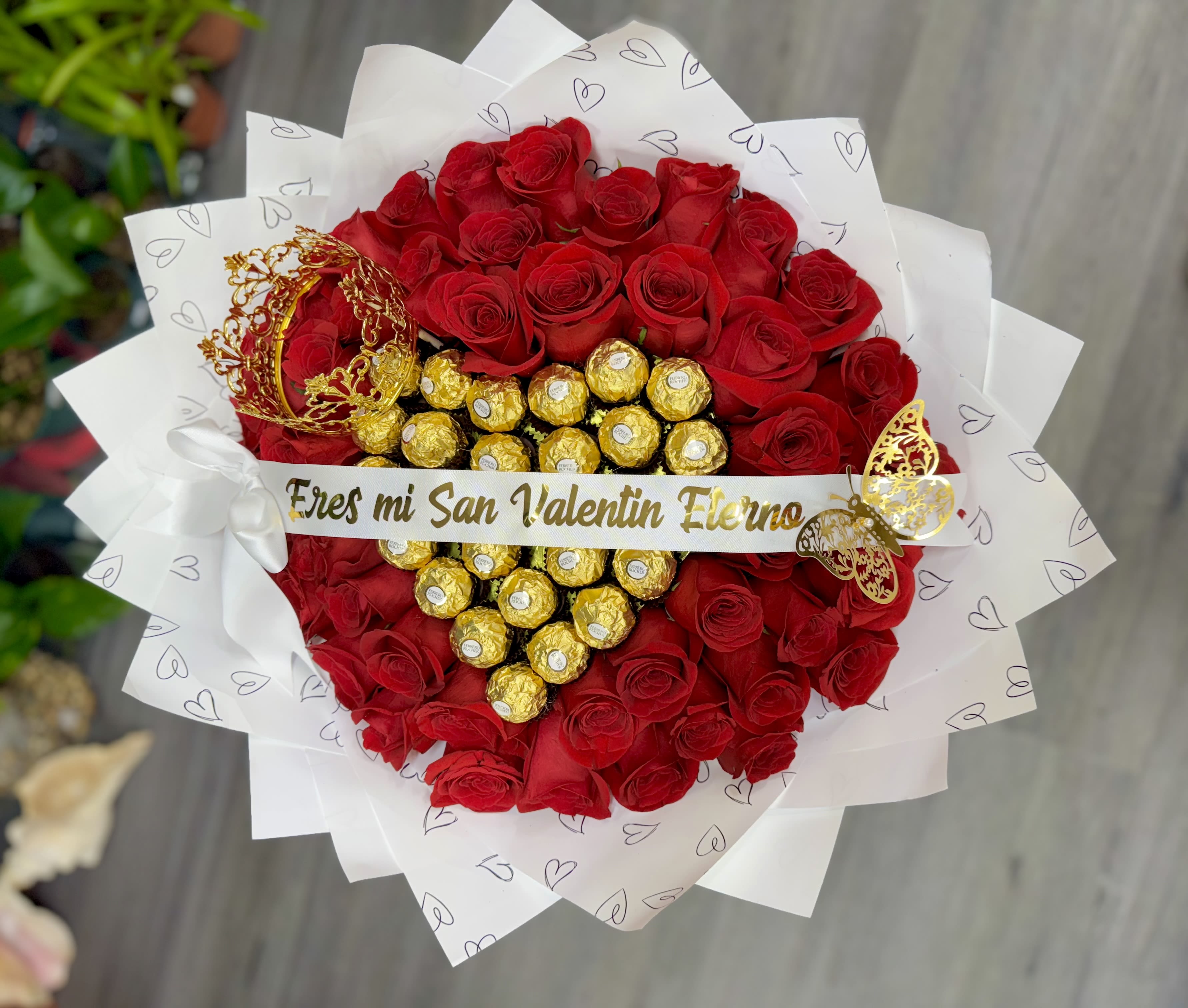 My Eternal Valentine” Personalized Bouquet – 50 Red Roses &amp; Chocolates - A stunning bouquet featuring 50 red roses, designed with a romantic chocolate heart centerpiece, a delicate decorative crown, and a customizable ribbon. The ribbon message can be personalized with phrases such as “Eres mi San Valentín eterno,” “You Are My Valentine,” or any special message of your choice. A perfect statement of love for Valentine’s Day, anniversaries, or unforgettable moments.