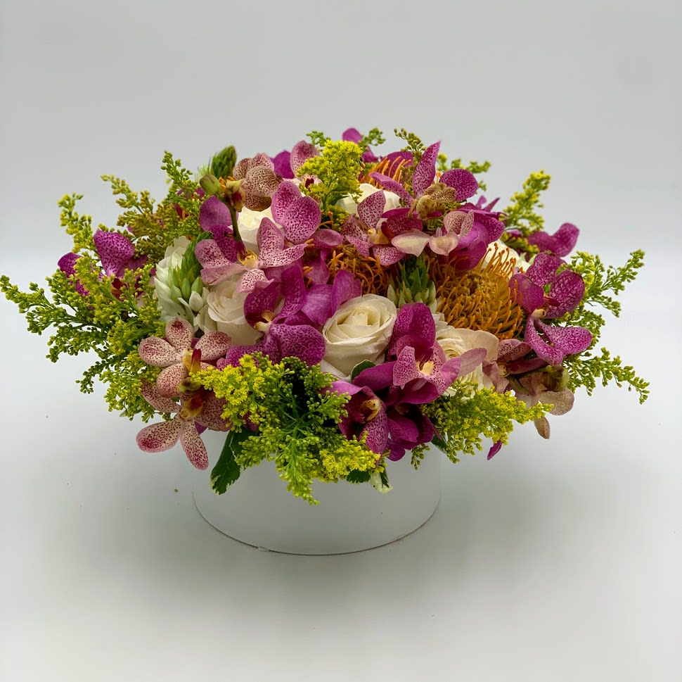 Tropical Garden  - like a trip to the middle east will leave you stunned and amazed so will this arrangement  A Combination of Purple Mokaras Orchids with white roses, Orange king Protea and Solidago, arranged in a white ceramic vase. 