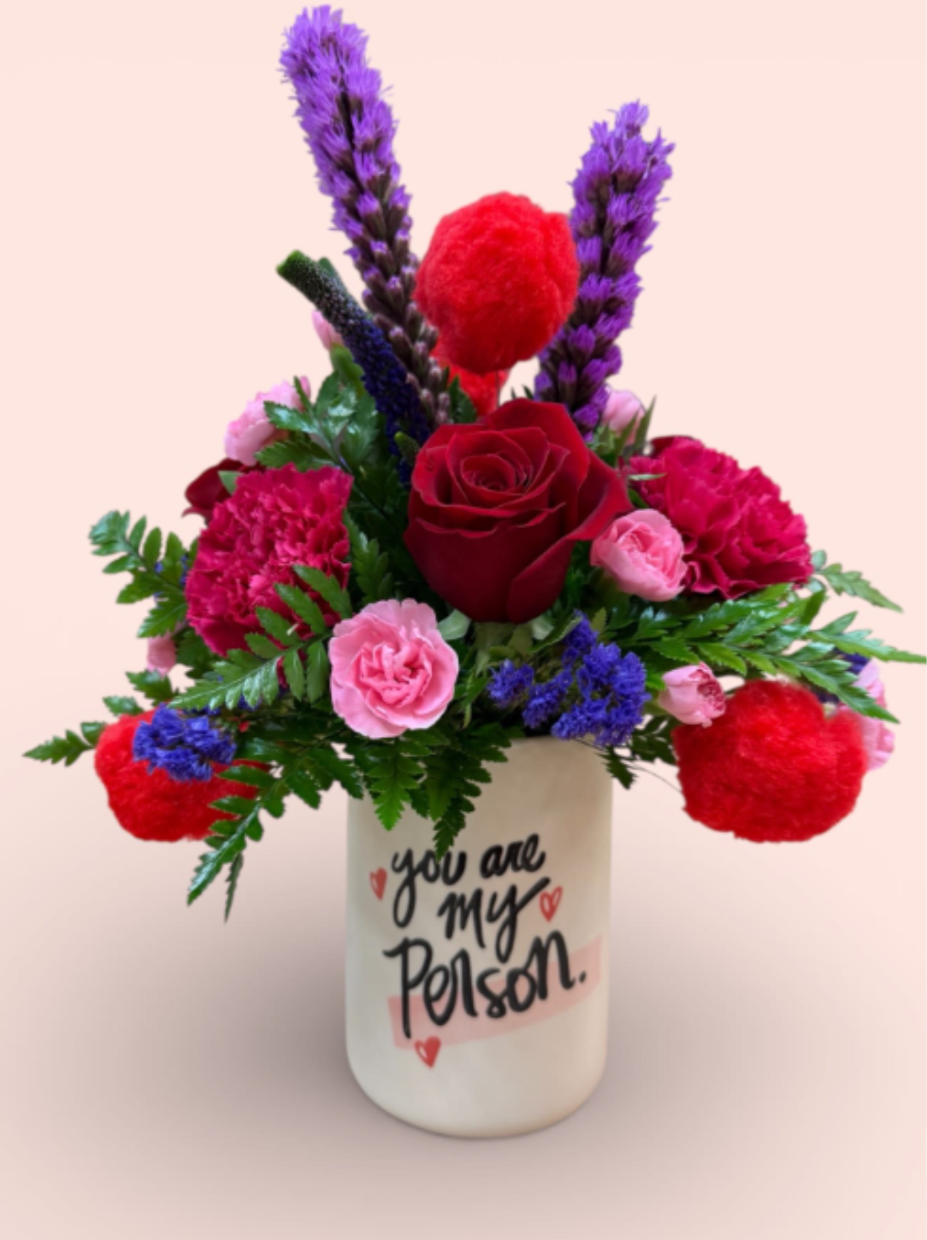 Encore - Our Encore arrangement steals the show with bold red roses, vibrant carnations, striking purple liatris, and playful bright red pompoms. Designed in a heartfelt ceramic pot reading “You are my person,” this Hollywood-inspired piece delivers romance, drama, and a standing ovation-worthy message—perfect for the one who’s always your co-star.
