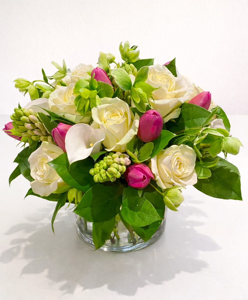 Blush Serenity - A graceful expression of softness and sophistication, Blush Serenity brings together a harmonious palette of gentle pinks, creamy whites, and fresh spring greens. This exquisite arrangement features velvety garden roses, elegant calla lilies, delicate tulips, and seasonal accent blooms, thoughtfully composed to create a design that feels both airy and refined.  Designed in a classic clear glass vase, the flowers are arranged with natural movement and texture, allowing each bloom to shine while forming a beautifully balanced silhouette. Perfect for celebrating life’s meaningful moments—whether a heartfelt thank-you, a warm welcome, or an elevated touch for the home or office.  Style: Elegant, soft, romantic Occasions: Sympathy, congratulations, corporate gifting, everyday luxury Care: Add fresh water every 1–2 days and keep in a cool location away from direct sunlight.  Let Blush Serenity deliver a message of quiet beauty and timeless charm.