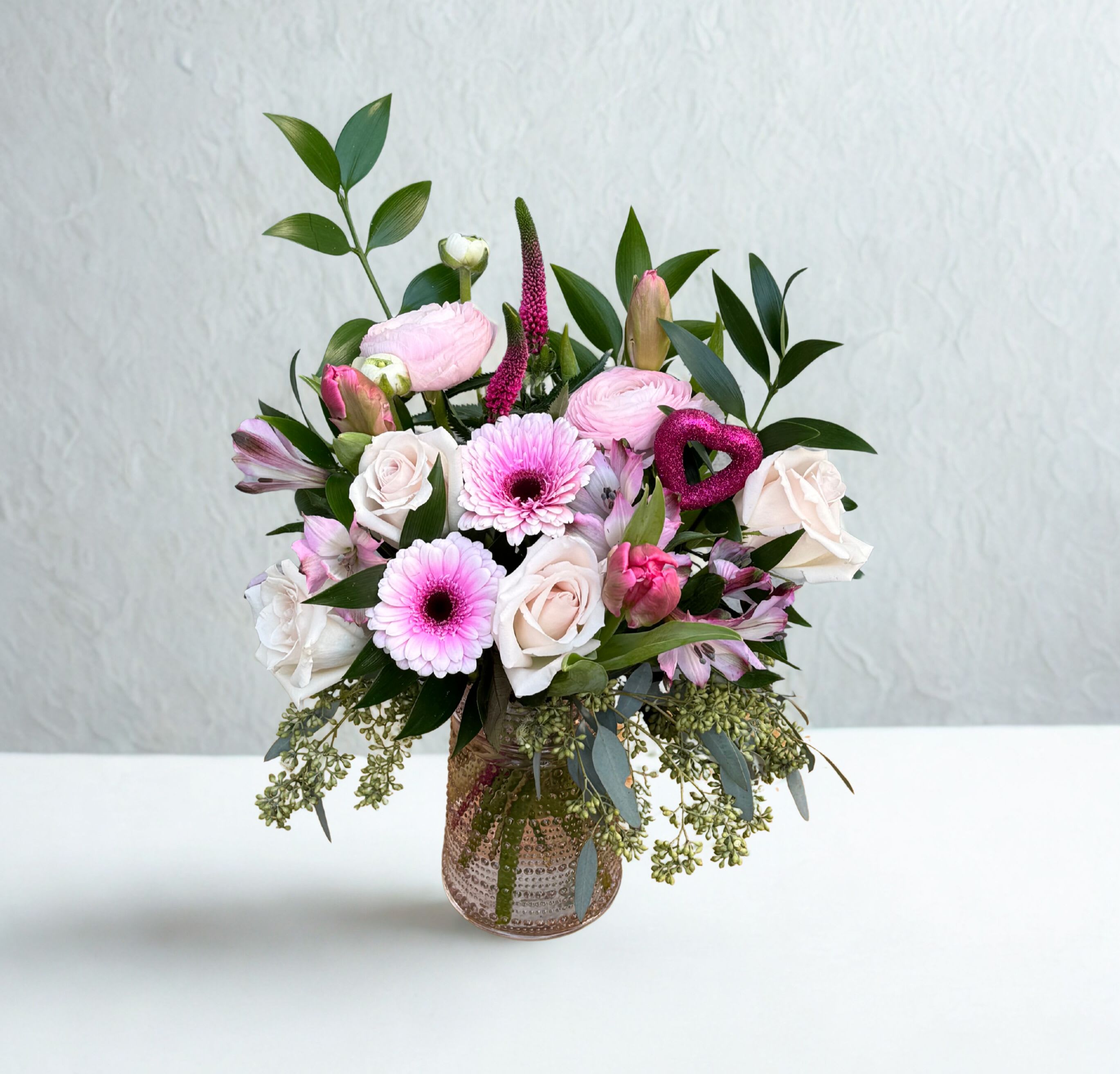 Hillsides Blushing Heart - This Valentine’s arrangement features creamy white and blush roses paired with cheerful pink blooms and fresh greens. Finished with a shimmering heart accent, it’s a charming way to say “you have my heart.”