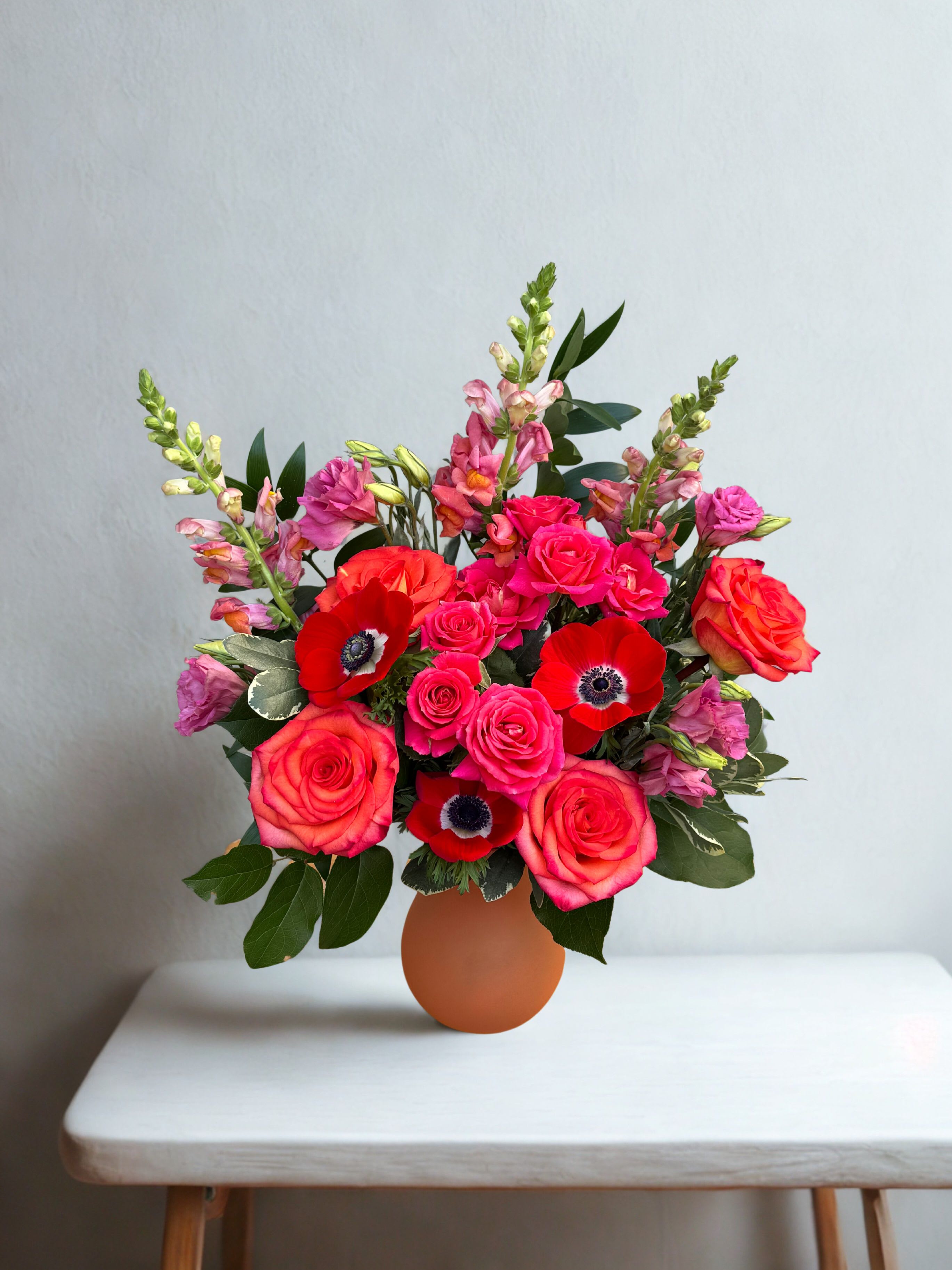Hillsides Orange you glad I love you!  - A romantic Valentine’s arrangement featuring lush red, pink, and coral blooms accented with fresh greenery. Classic roses and striking anemones come together in a warm, modern vase to create a bold yet elegant expression of love—perfect for saying “I love you.”