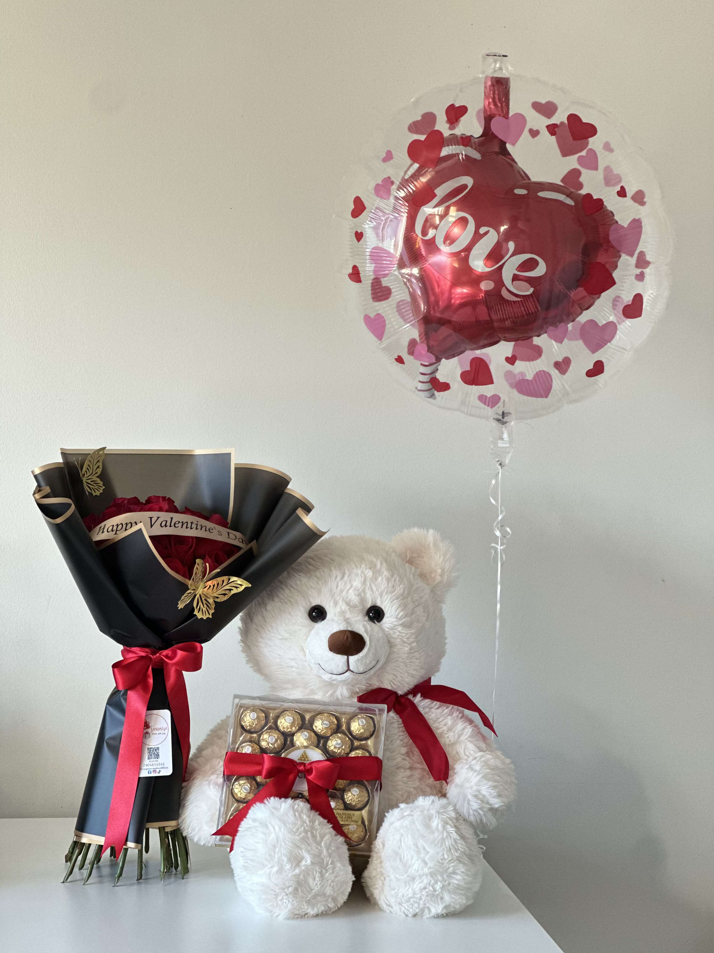 Be Mine - Bouquet of 24 roses and ribbon with "Happy Valentine's Day" message, 20" teddy bear, box of Ferrero Rocher, 24" helium balloon. This all-in-one gift is curated to deliver smiles and sweetness straight to their door. Bouquet de 24 rosas y cinta con mensaje "Happy Valentines Day", peluche de 20', caja de Ferrero Rocher, globo de 24" con helio.