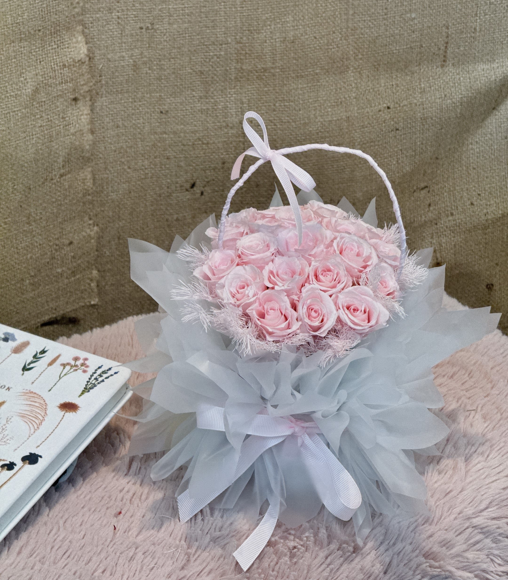 Gentle Joy - This is a very exquisite small pink rose, white and the whole presents an elegant basket shape. The pink roses are closely arranged, with transparent wrapping paper and large white bows, making the whole bouquet look both romantic and layered.