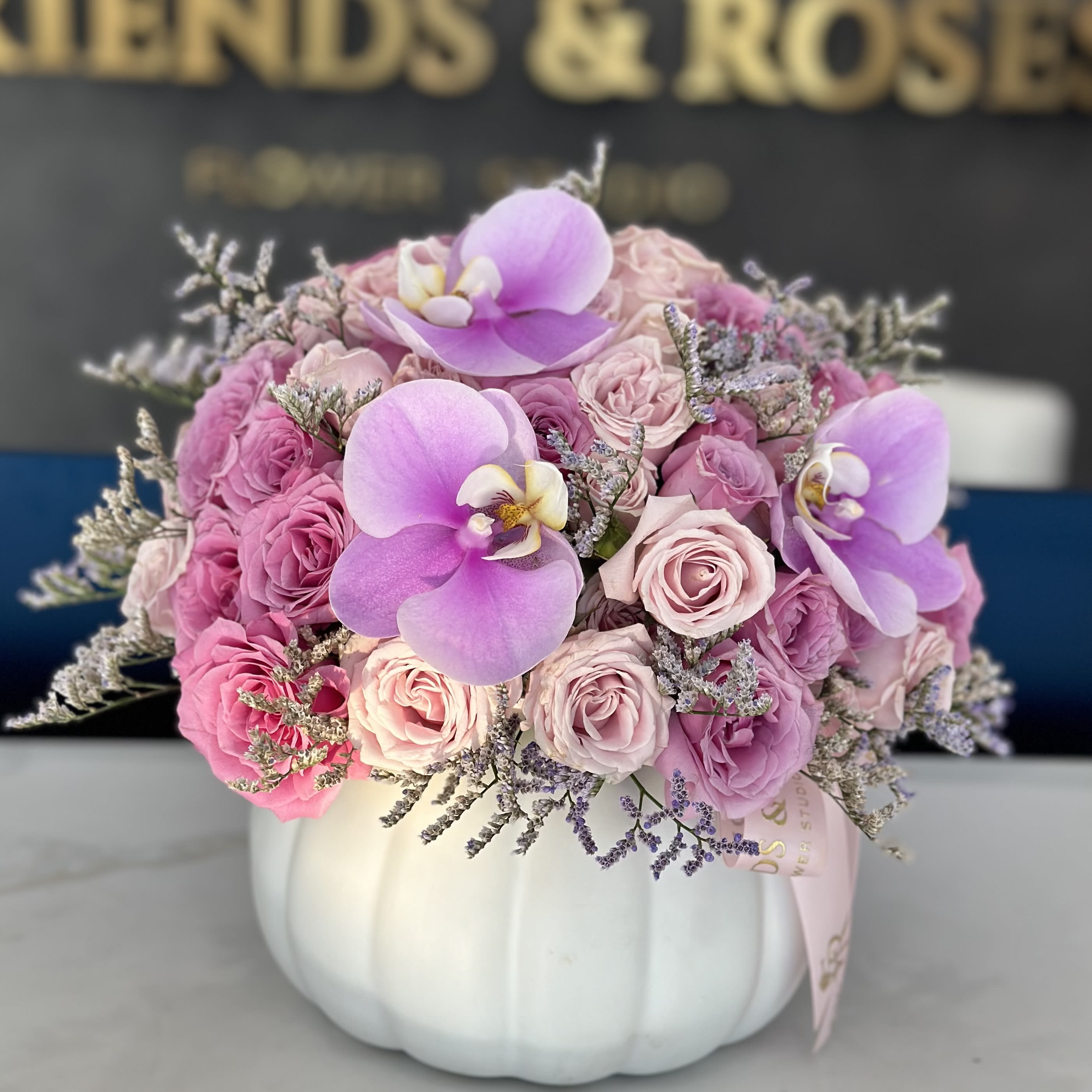 Autumn Charm - A sweet , elegant bouquet in a white pumpkin , featuring soft pink and purple roses accented with delicate orchids. This arrangement combines seasonal charm with a touch of sophistication.