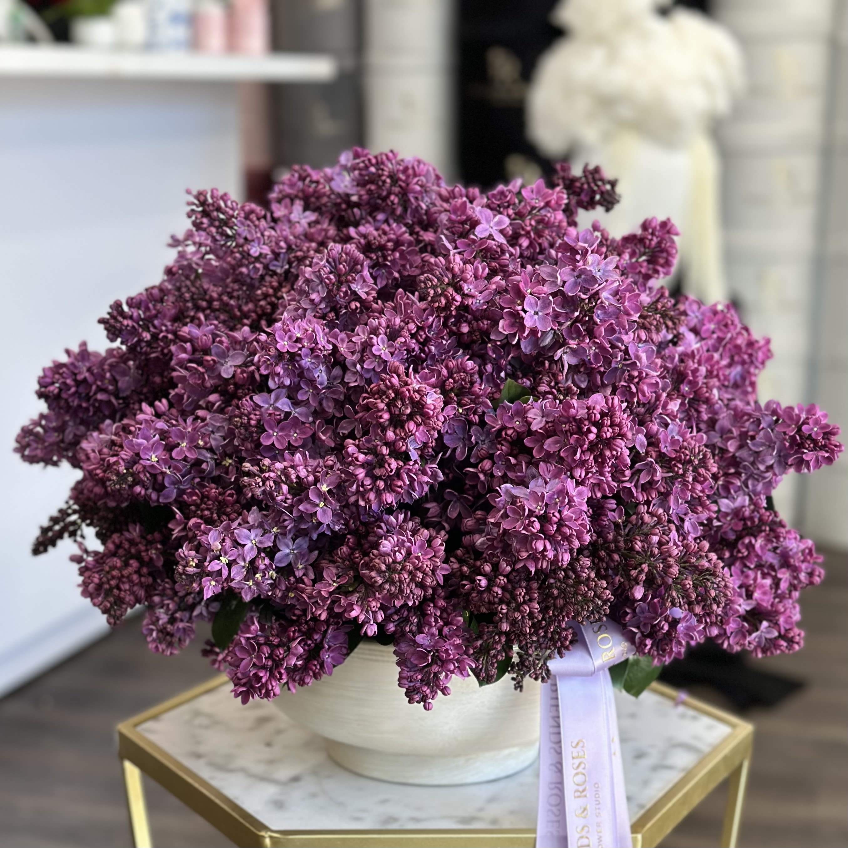 Cloud of lilac. - An airy composition of lilacs in a low antique vase radiates effortless elegance, with fragrant blooms gently arching outward in soft, natural waves. The vintage vessel adds a touch of history, enhancing the lilacs' delicate, nostalgic beauty.
