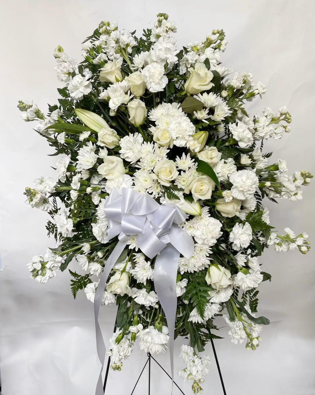 A Pure Blessing - This Pure Blessings picks exclusively white and green to elegantly presented the sweet serenity. It's an outstanding way to honor the life of your loved one.   Ingredients: White roses, Asiatic lilies, chrysanthemums and mini carnations, palm fronds and lush greens, with a white satin ribbon  Vase: Presented on a wire easel Size: Standard, Approximately 32"h*20"w Deluxe, Approximately 33"h x 21"w Premium, Approximately 34"h*22"w
