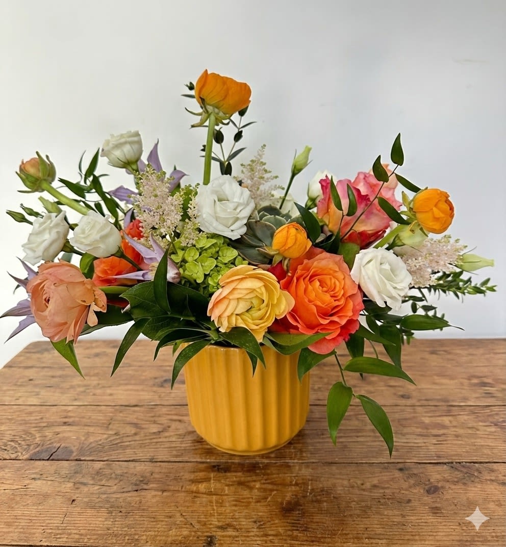 Spring breeze - This arrangement features a very bright spring color. It is presented in a 4.5" yellow ceramic cylinder vase. The arrangement includes seasonal ranunculus, orange garden roses, green hydrangea, white lisianthus, pastel astilbe, green hydrangea with assorted greens. 